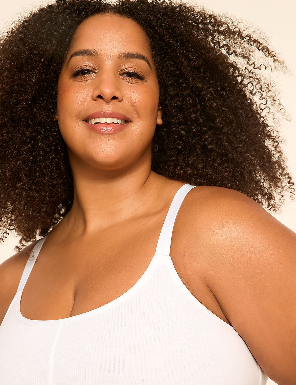 A smiling woman with curly dark hair wears a white top in the foreground, against a plain, light-colored background. Product Image 4