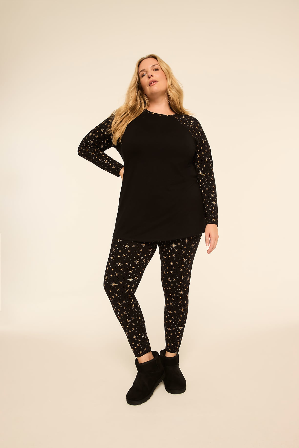 A woman in a black long-sleeved shirt with star-patterned sleeves and matching leggings stands against a plain, light-colored background. Product Image 5