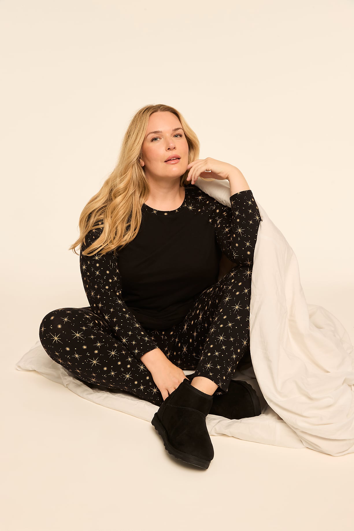 A woman in star-patterned pajamas and slippers sits on a plain background, partially covered by a white blanket. Product Image 7
