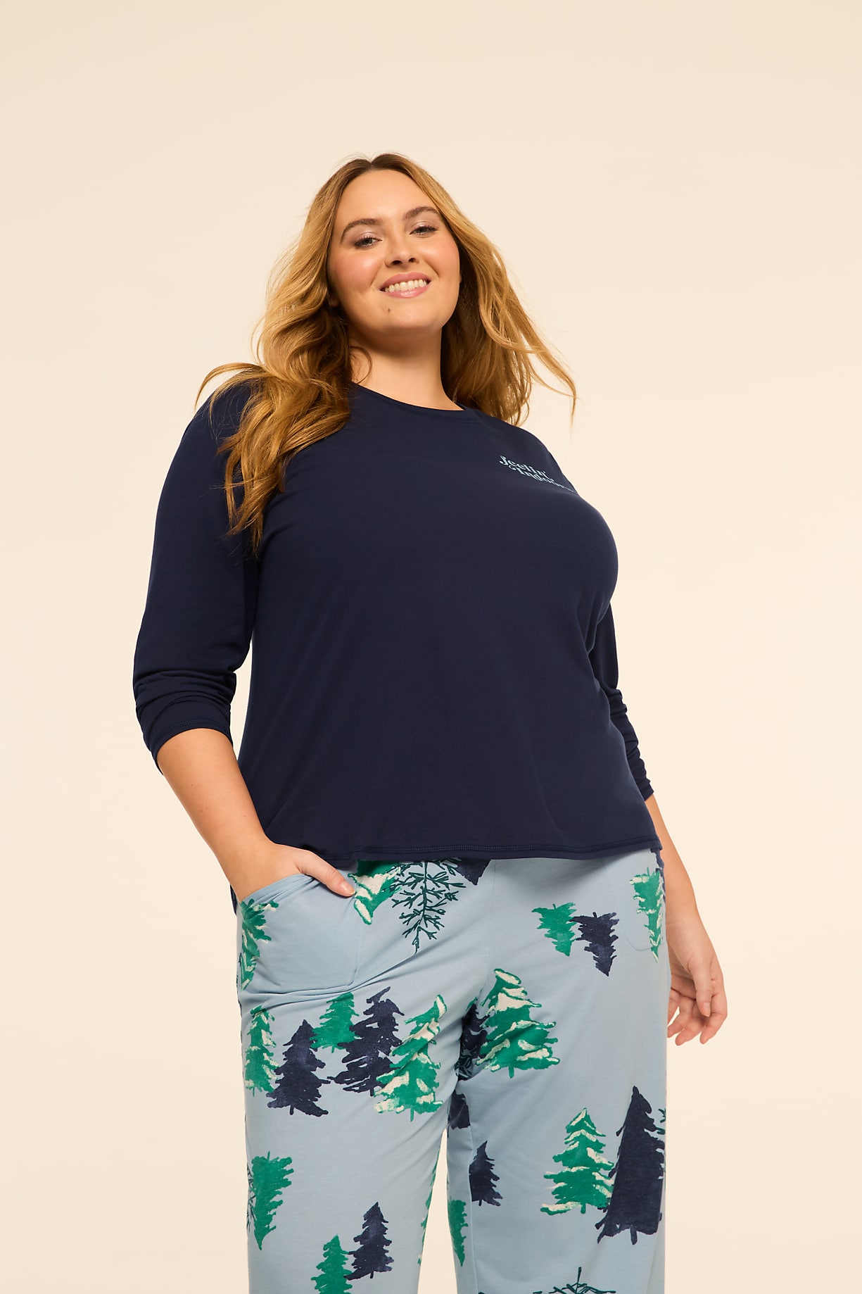 A smiling woman in a navy blue shirt and light blue pajama pants with a forest print stands against a plain, light-colored background. Product Image 7