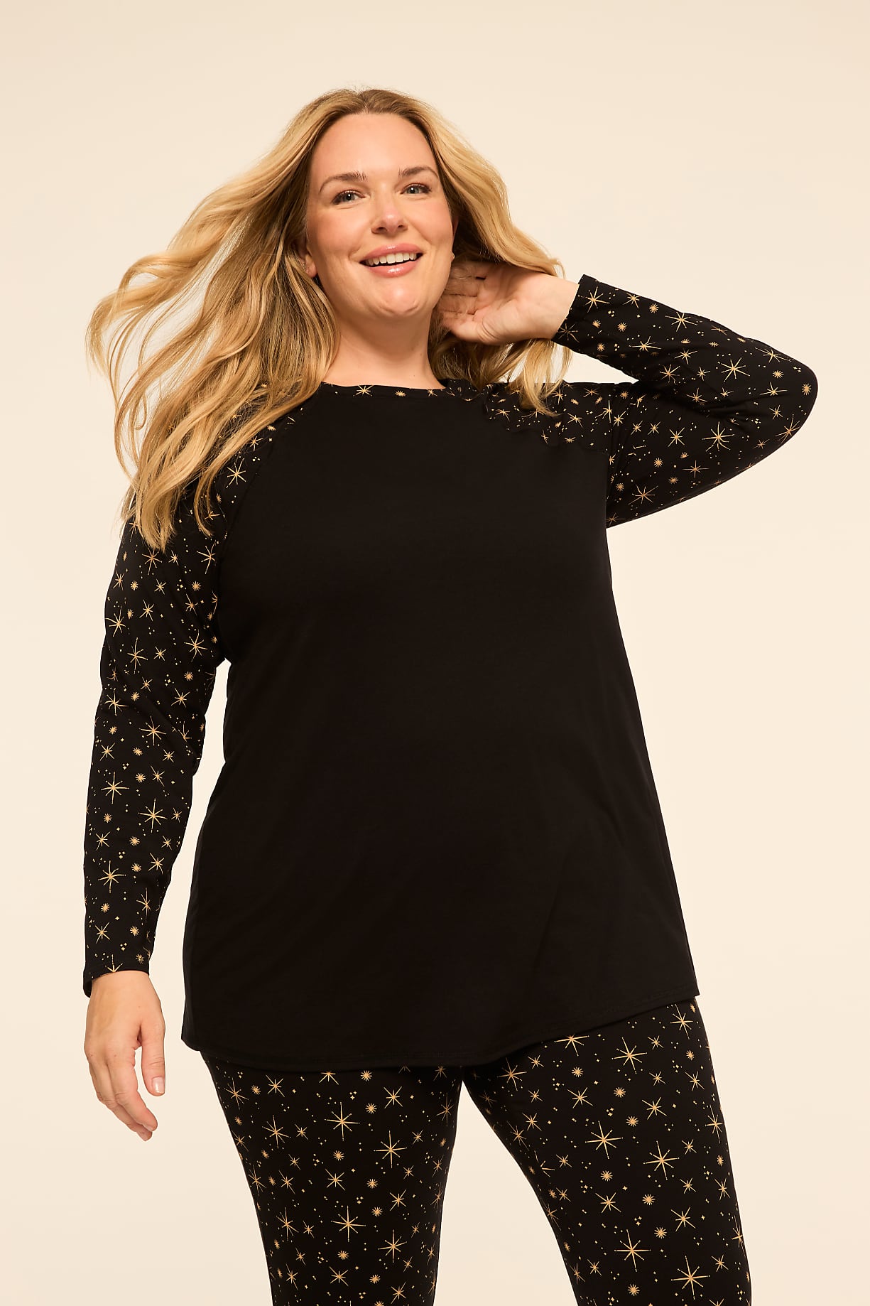 A smiling woman with blonde hair poses in a black top with star-patterned sleeves and matching pants against a plain, light-colored background. Product Image 9