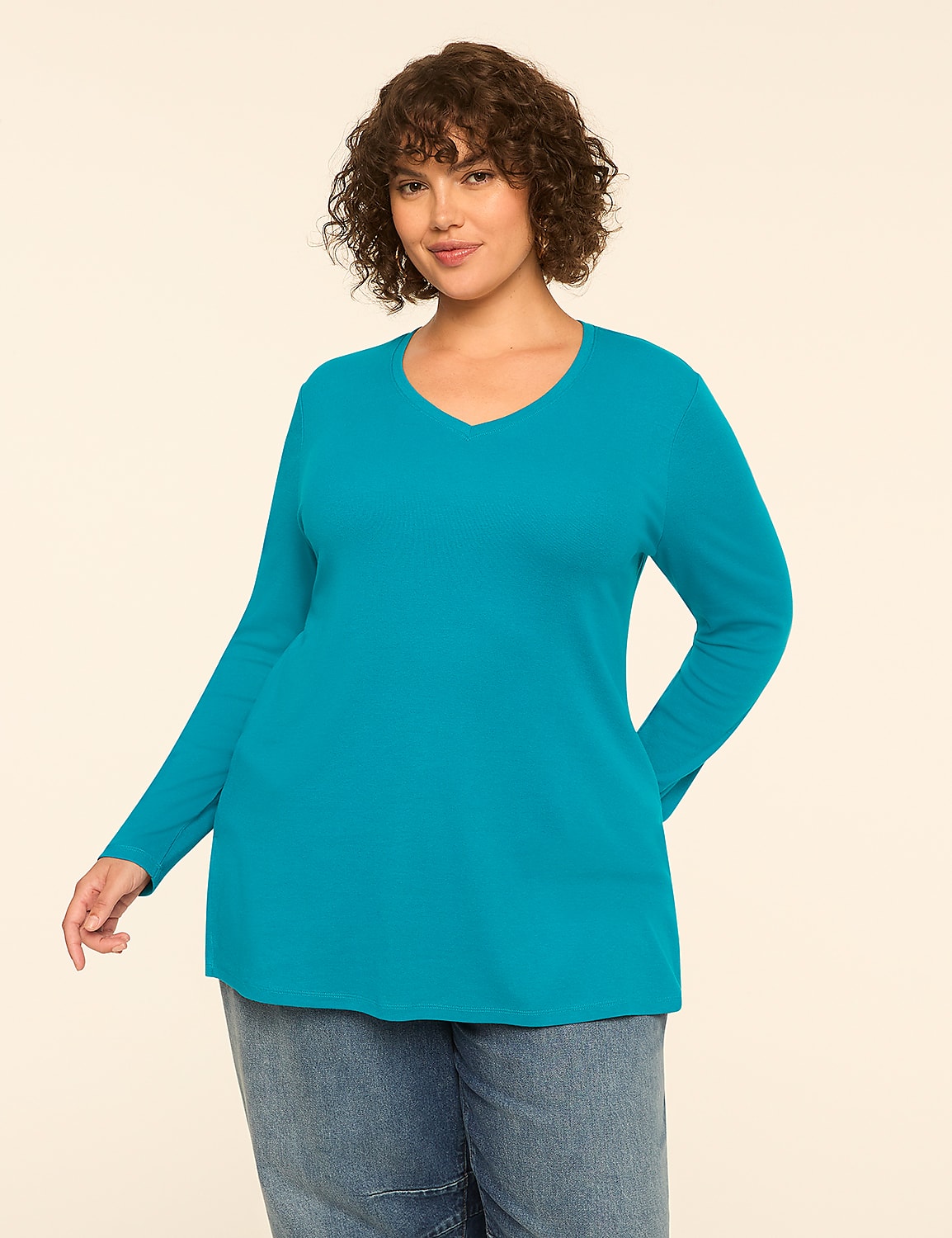 A woman with curly brown hair and a v-neck teal long-sleeved shirt stands in front of a plain cream background. Product Image 1