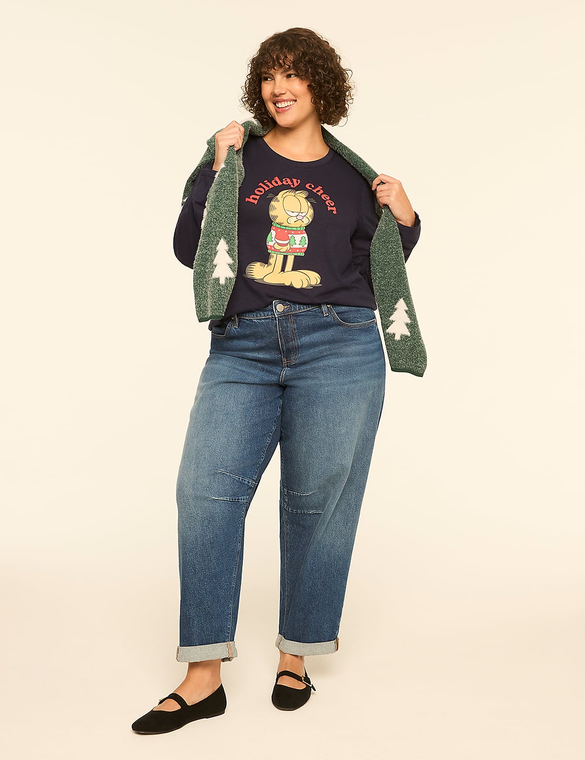 A woman in a Garfield holiday sweater and jeans stands against a plain cream background, holding a green scarf with Christmas trees. Product Image 3
