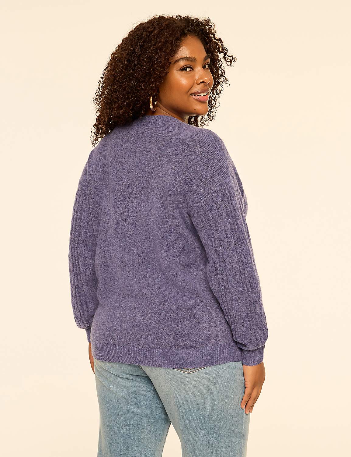 A woman with curly hair wearing a purple sweater and light blue jeans stands against a plain, light-colored background. Product Image 2