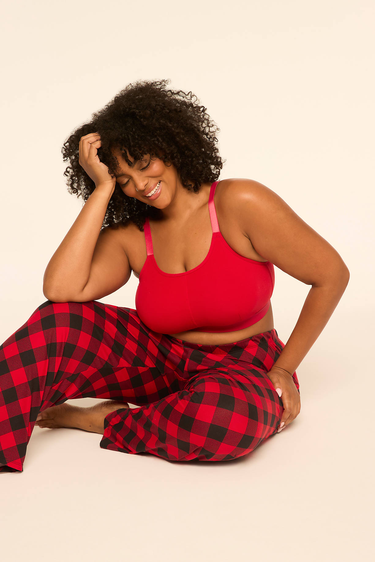 A smiling woman with curly hair wearing a red bra and red-and-black plaid pants sits on a plain, light-colored background. Product Image 5