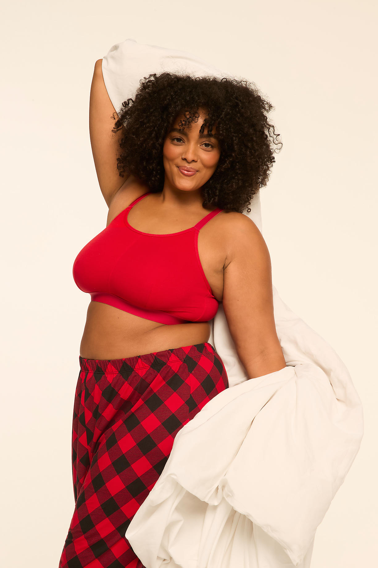 A woman with curly hair wearing a red top and red-and-black checkered pajama pants holds a white duvet against a plain white background. Product Image 6