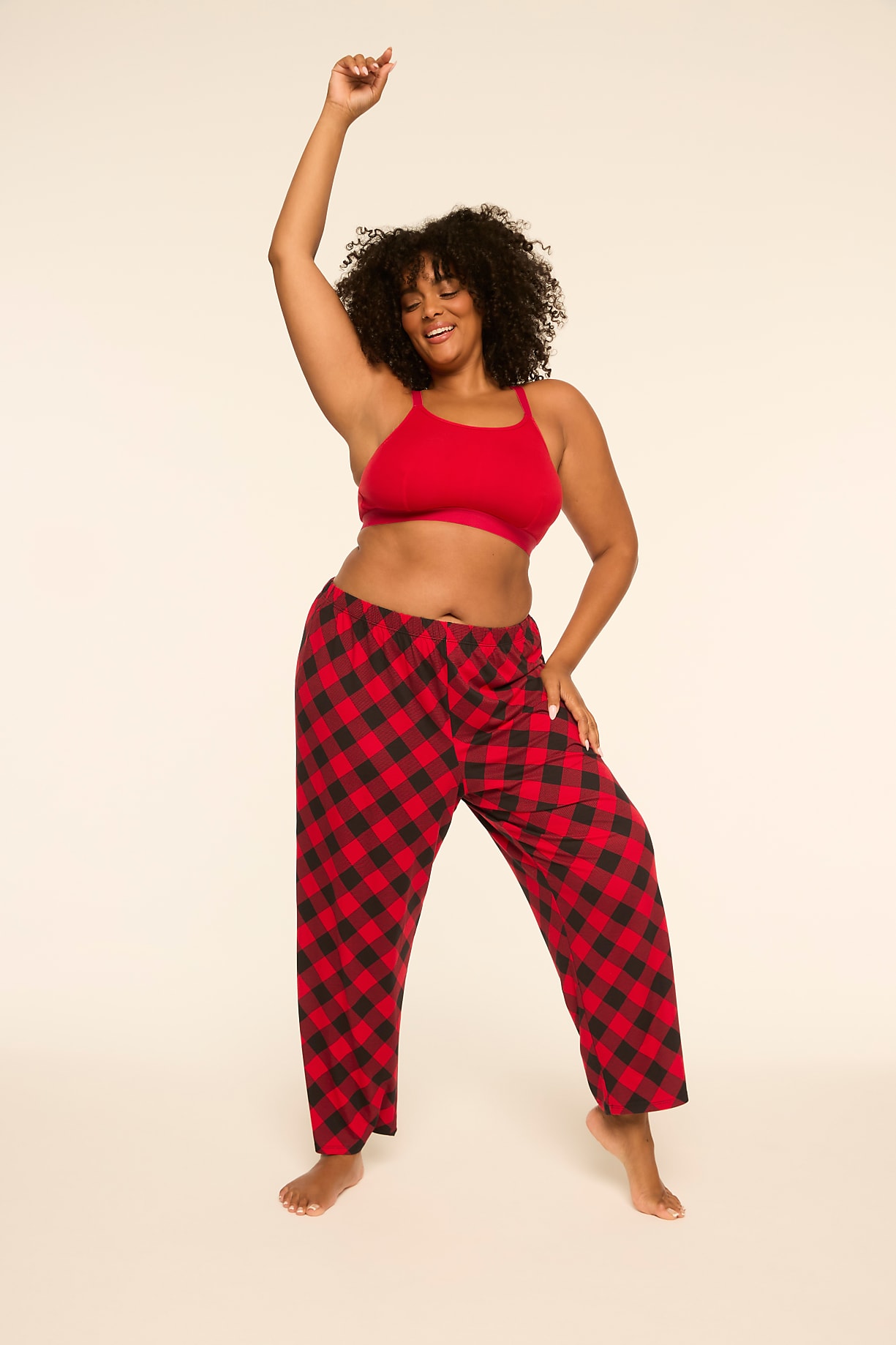 A smiling woman with curly hair wearing a red top and red-and-black checkered pants poses against a plain, light-colored background. Product Image 8