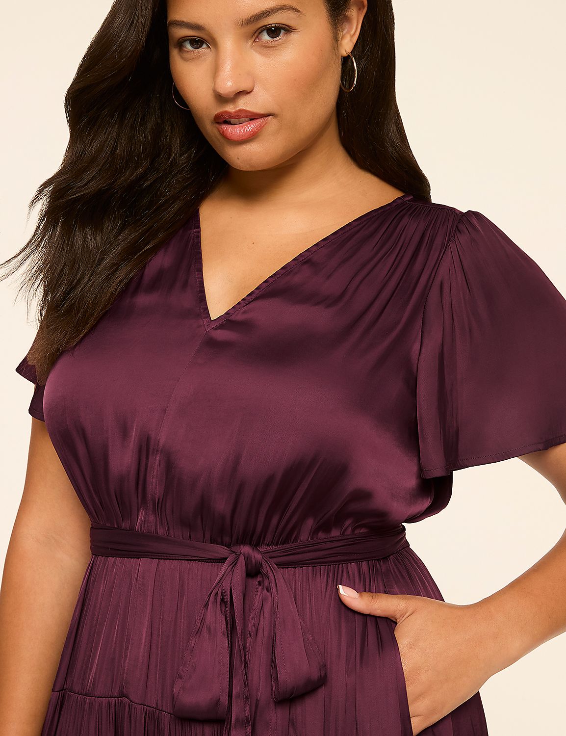 A woman in a burgundy satin dress with flutter sleeves and a tie waist stands against a plain, light-colored background. Product Image 3
