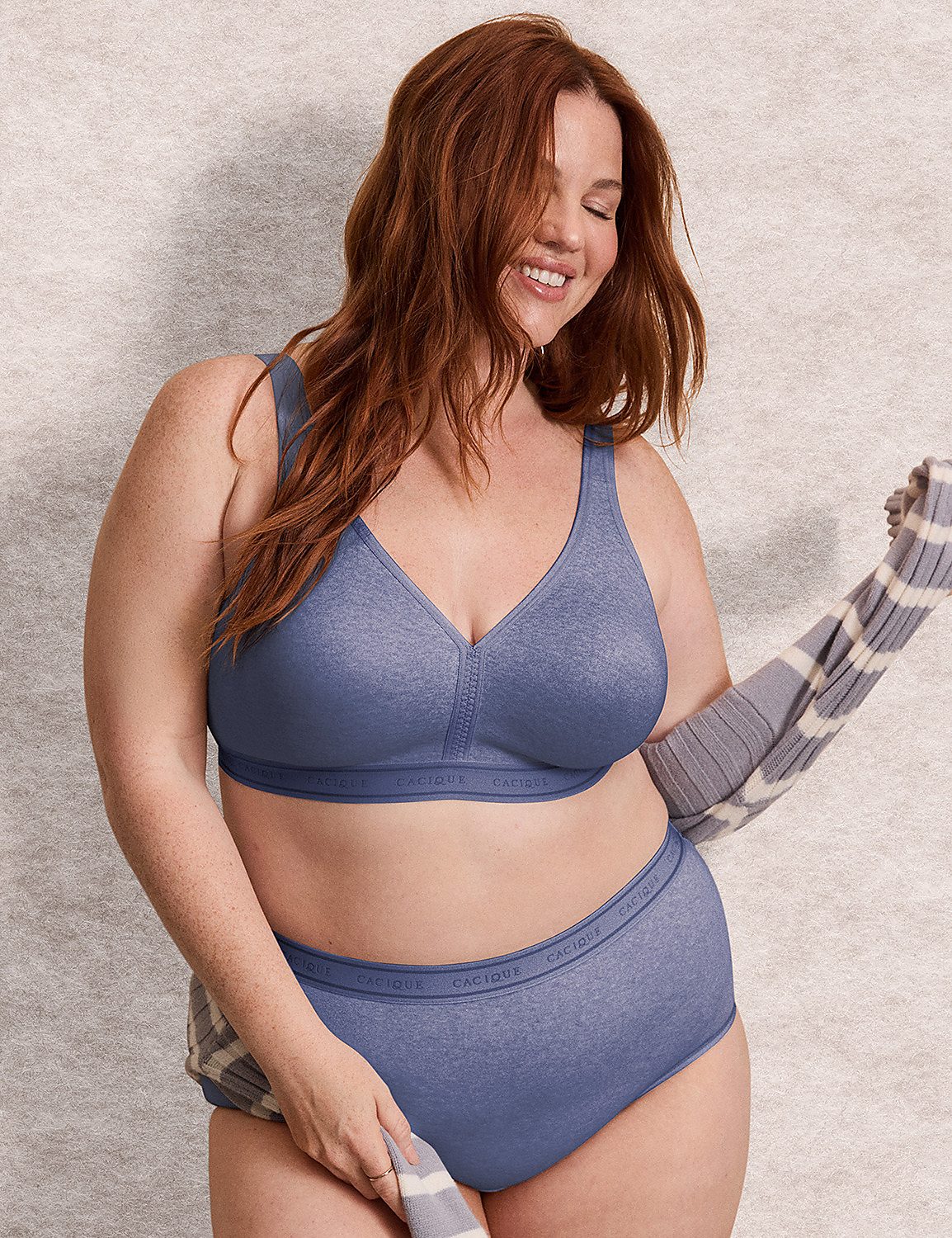A smiling woman with red hair wears a blue lingerie set and a grey-and-white striped cardigan against a neutral, textured background. Product Image 5