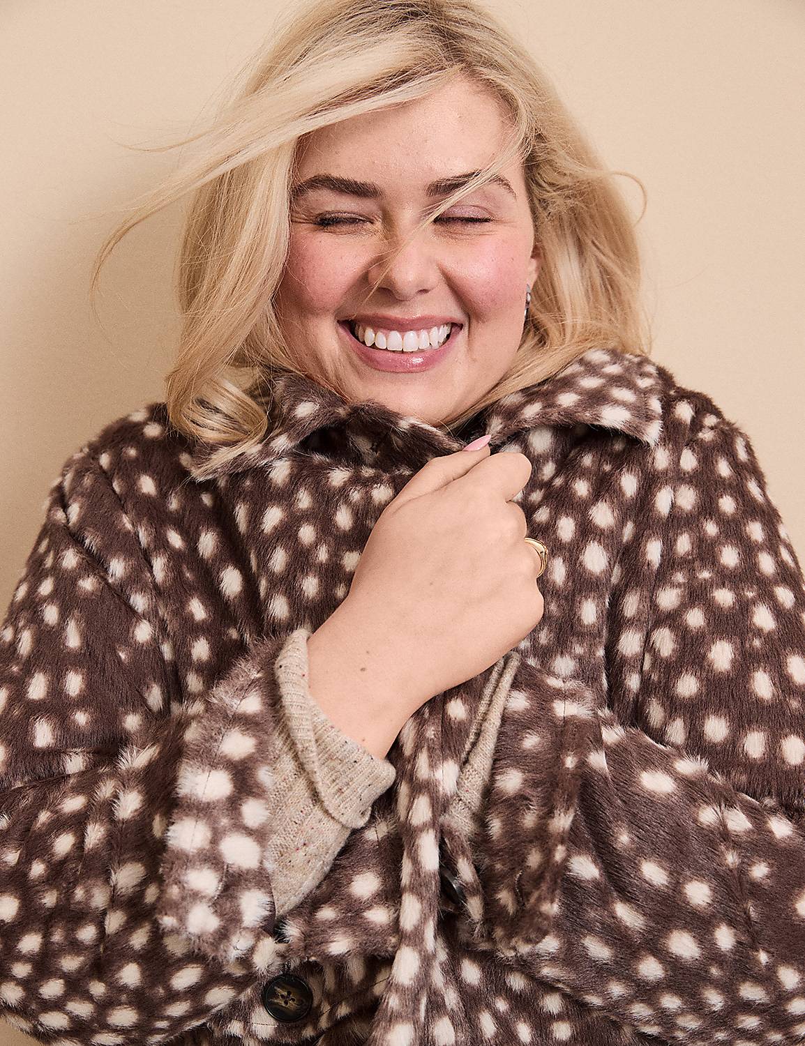 A smiling blonde woman wearing a brown and white spotted faux-fur coat stands against a plain, neutral-toned background. Product Image 4