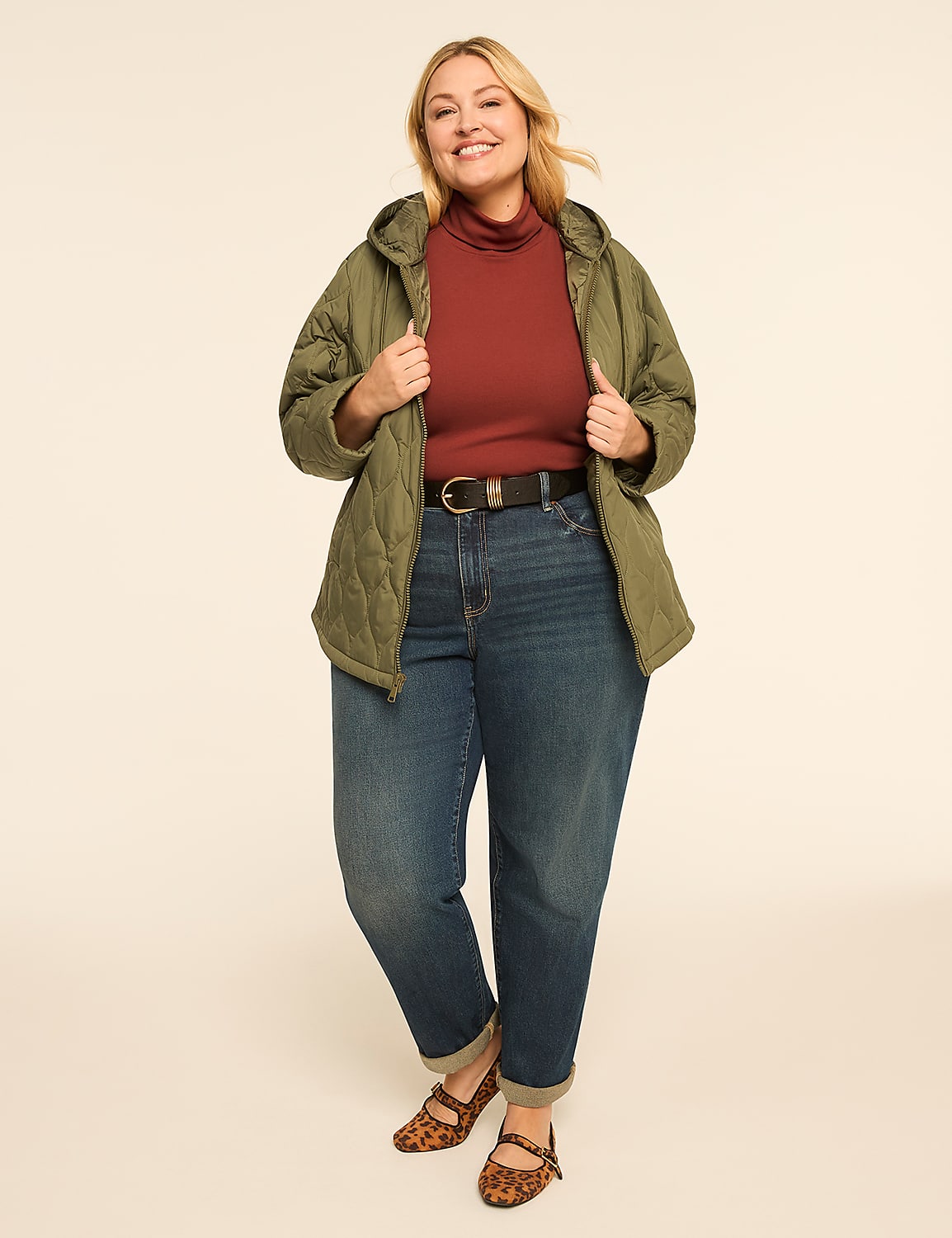 A smiling woman in a quilted green jacket, rust turtleneck, and cuffed jeans stands against a plain, light-colored background. Product Image 3