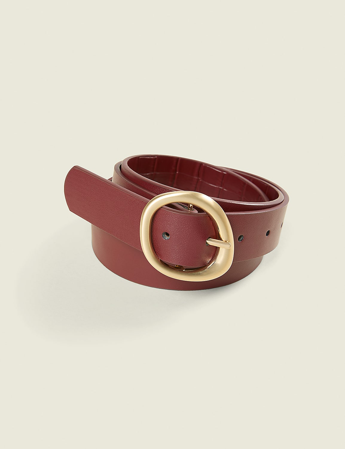 A rolled burgundy leather belt with a gold oval buckle sits against a plain, light beige background. Product Image 1
