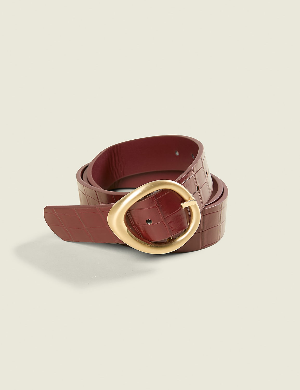 A burgundy croc-embossed leather belt with a gold oval buckle rests on a plain, light beige background. Product Image 2