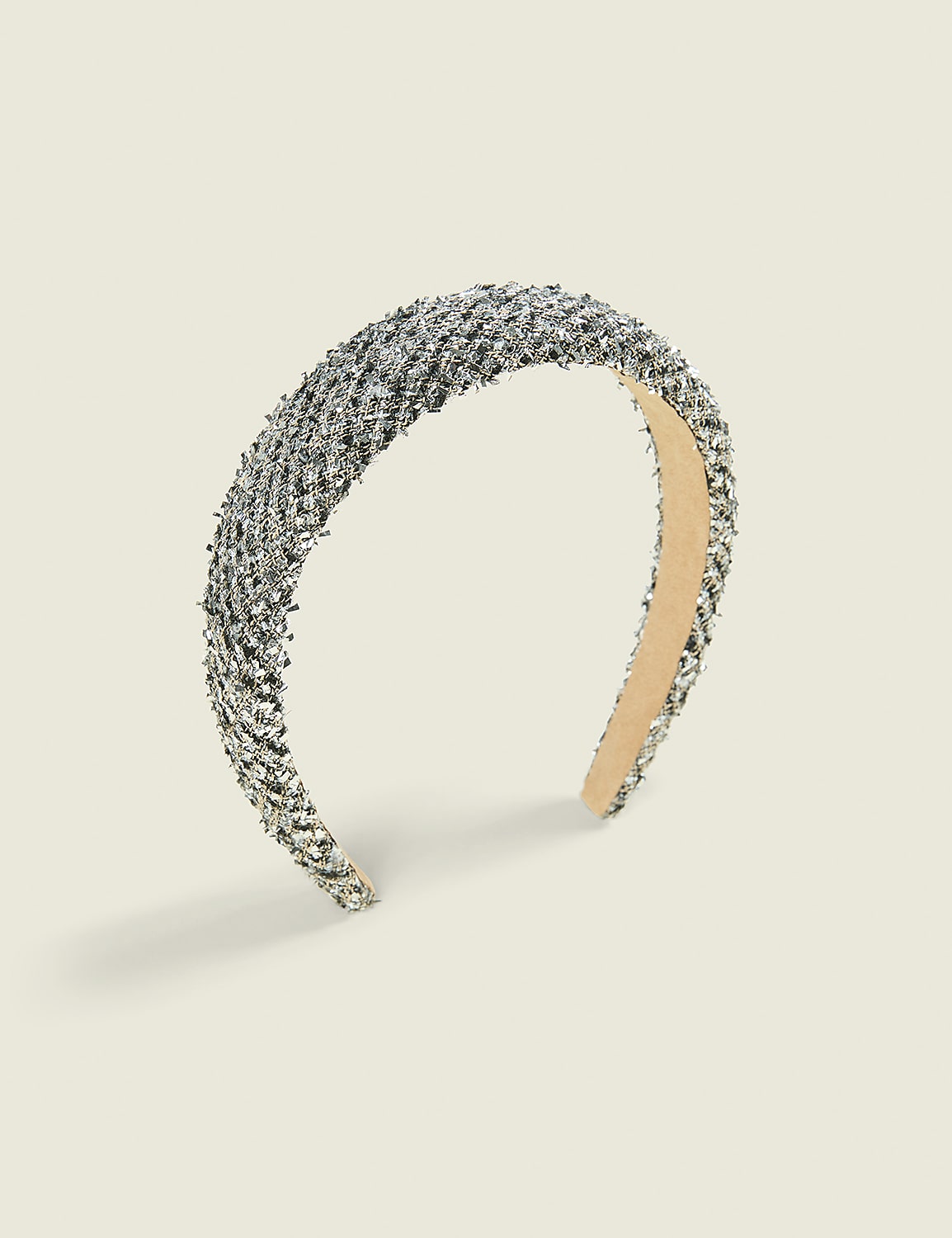A silver glittery headband sits centered against a plain, light beige background. Product Image 1