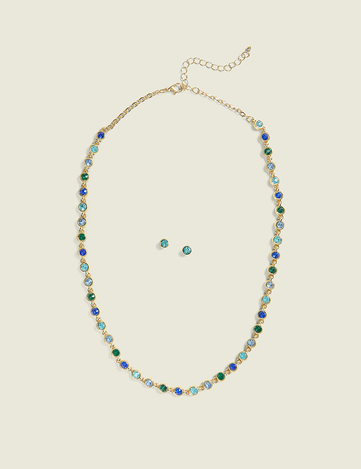 A gold necklace with blue and green gemstones and matching stud earrings are centered on a plain, light beige background. Product Image 1