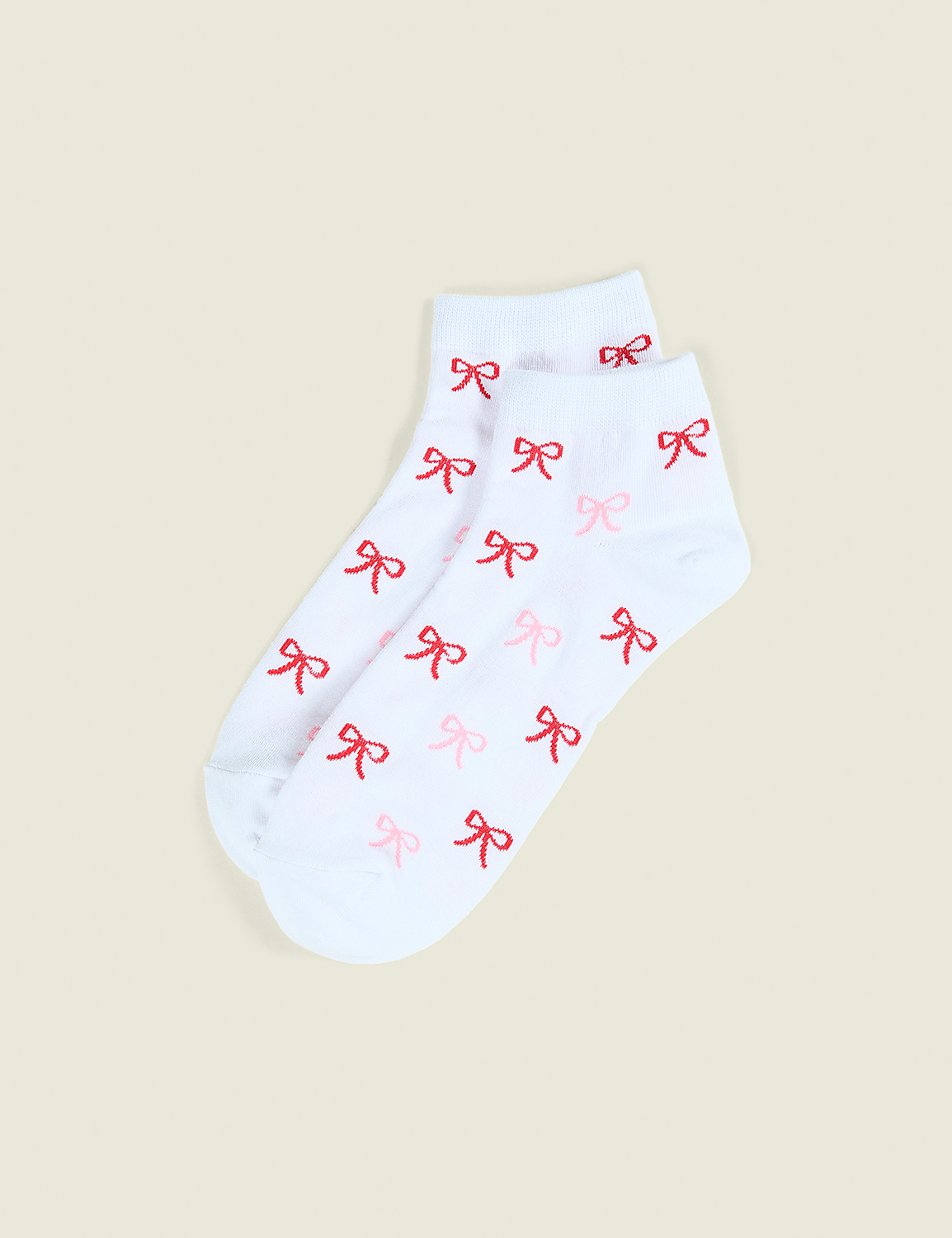 A pair of white socks with small red bows are laid flat against a plain, light beige background. Product Image 1