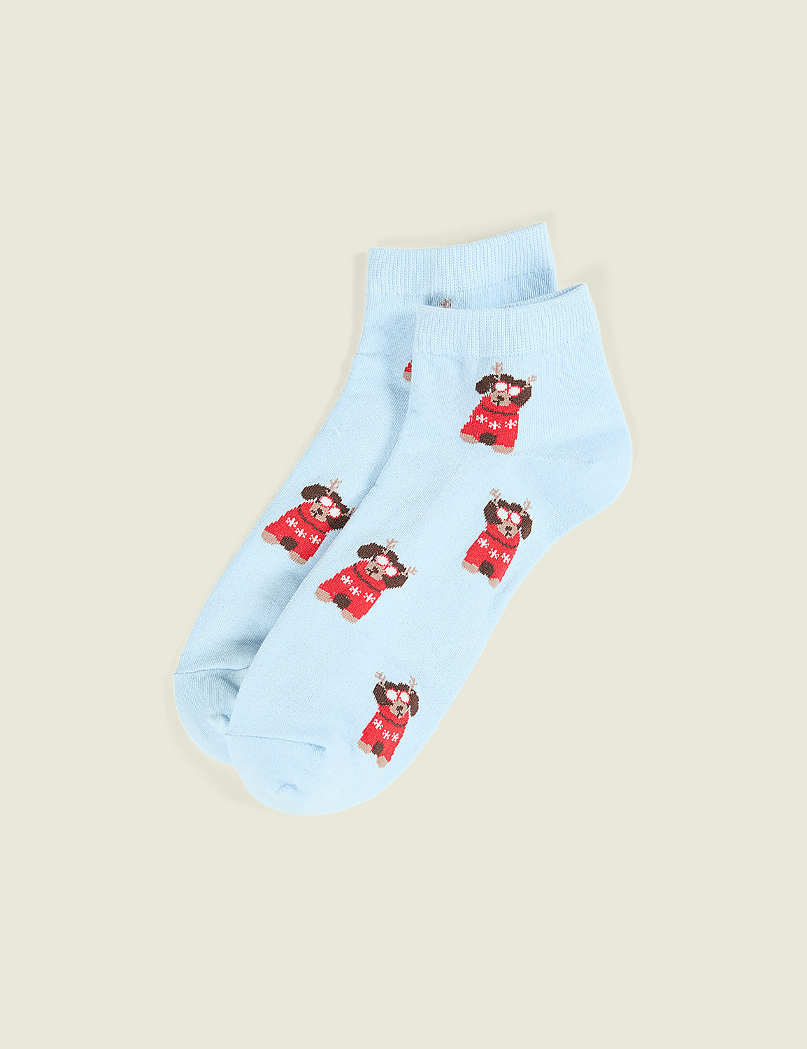 A pair of light blue socks featuring small reindeer in red sweaters rests on a plain, neutral beige background. Product Image 1