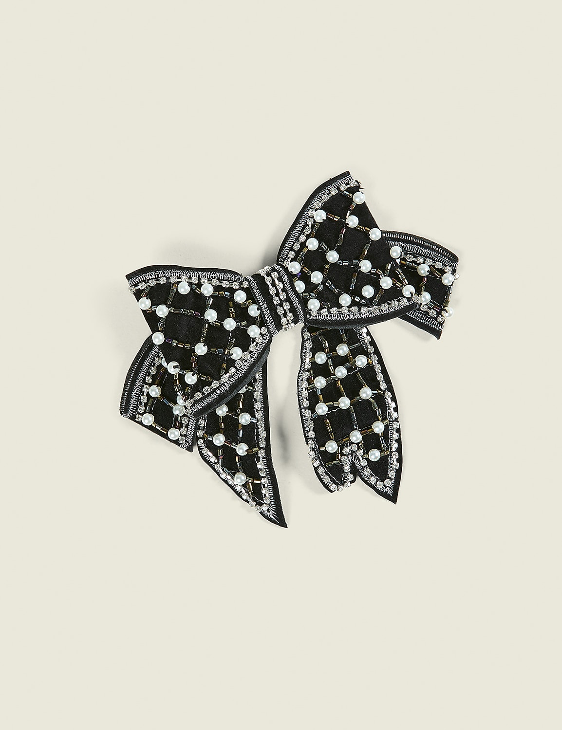 A black bow embellished with pearls and silver sequins rests on a plain, light beige background. Product Image 1