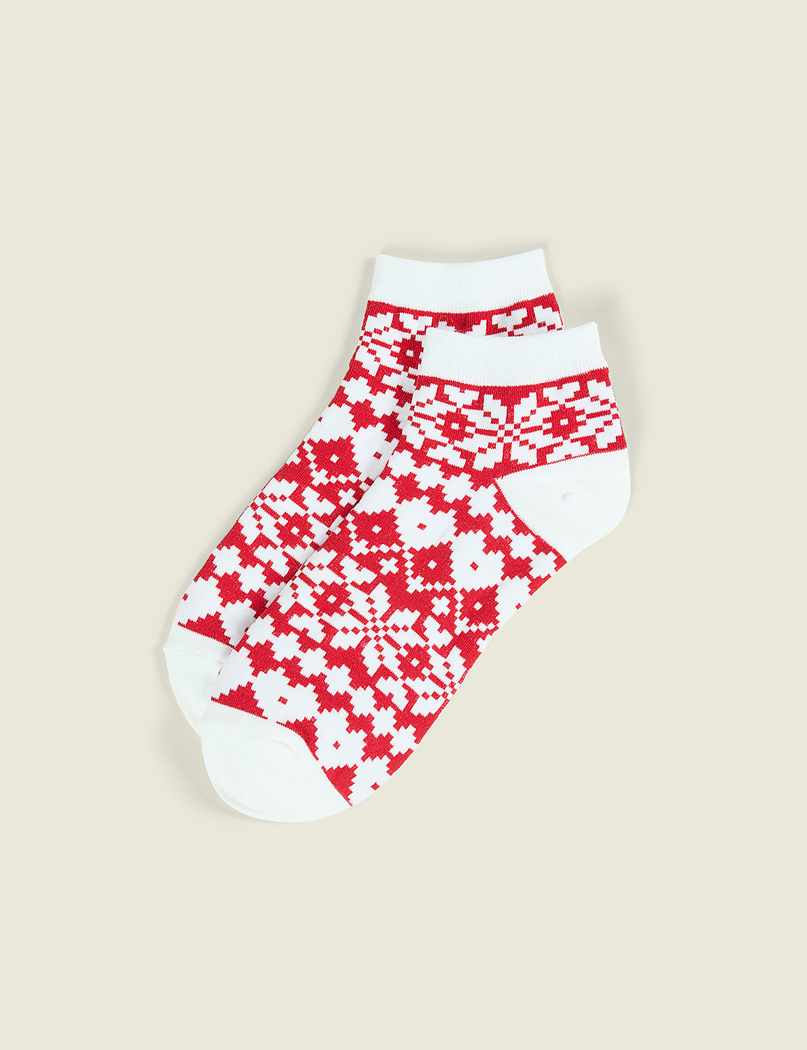 A pair of white socks with red Fair Isle patterns lies on a plain, light beige background. Product Image 1