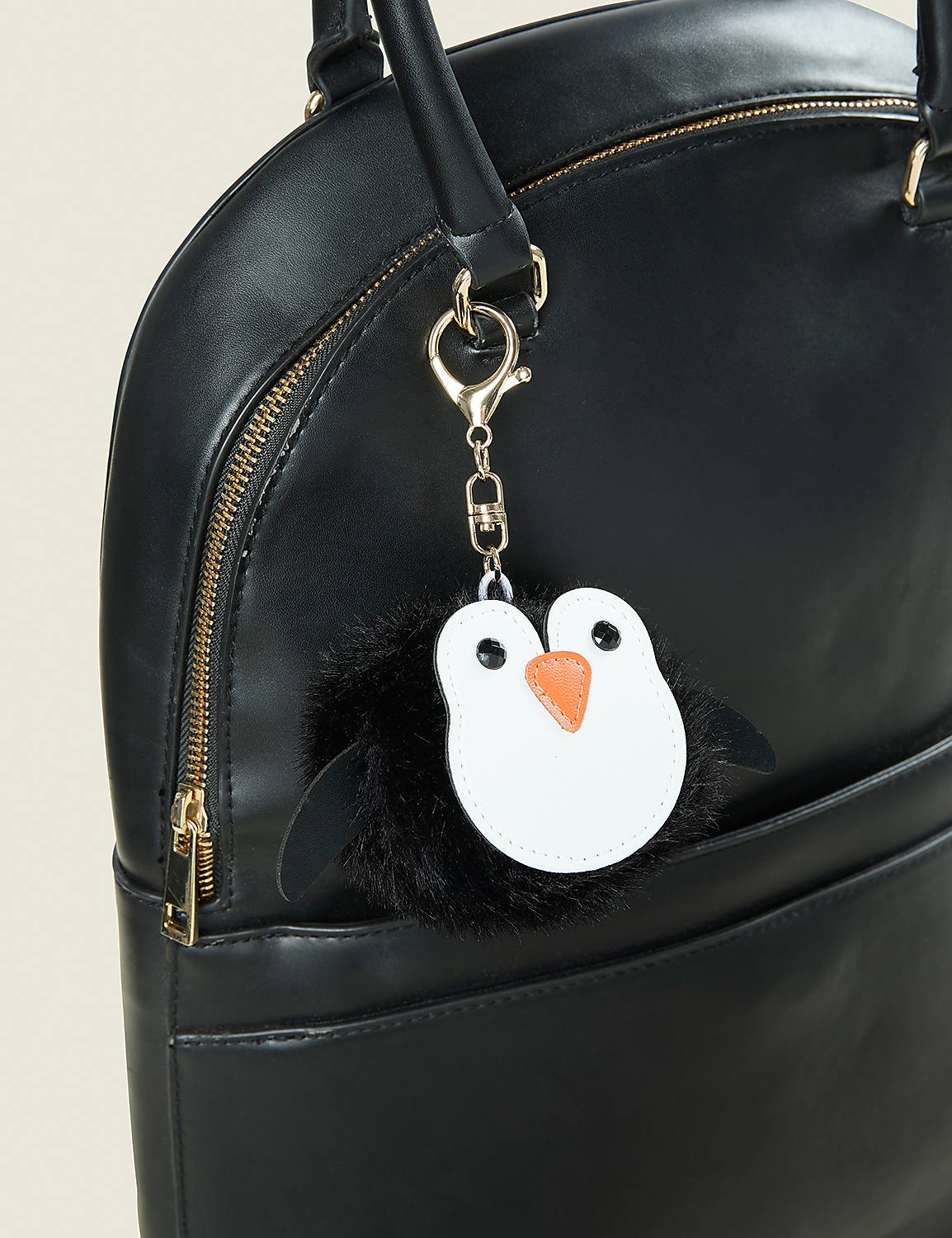 A fluffy penguin charm hangs from the handle of a sleek black leather handbag against a plain light background. Product Image 2