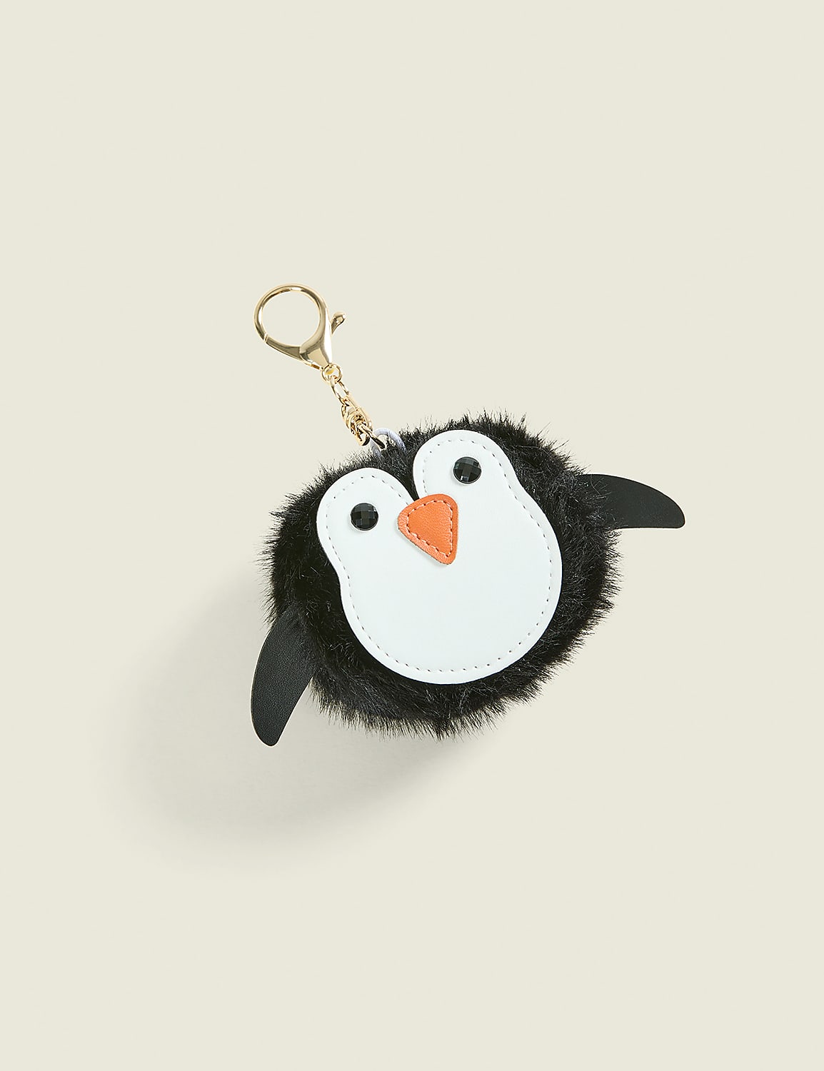 A fluffy black and white penguin keychain with an orange beak sits against a plain, light beige background. Product Image 1