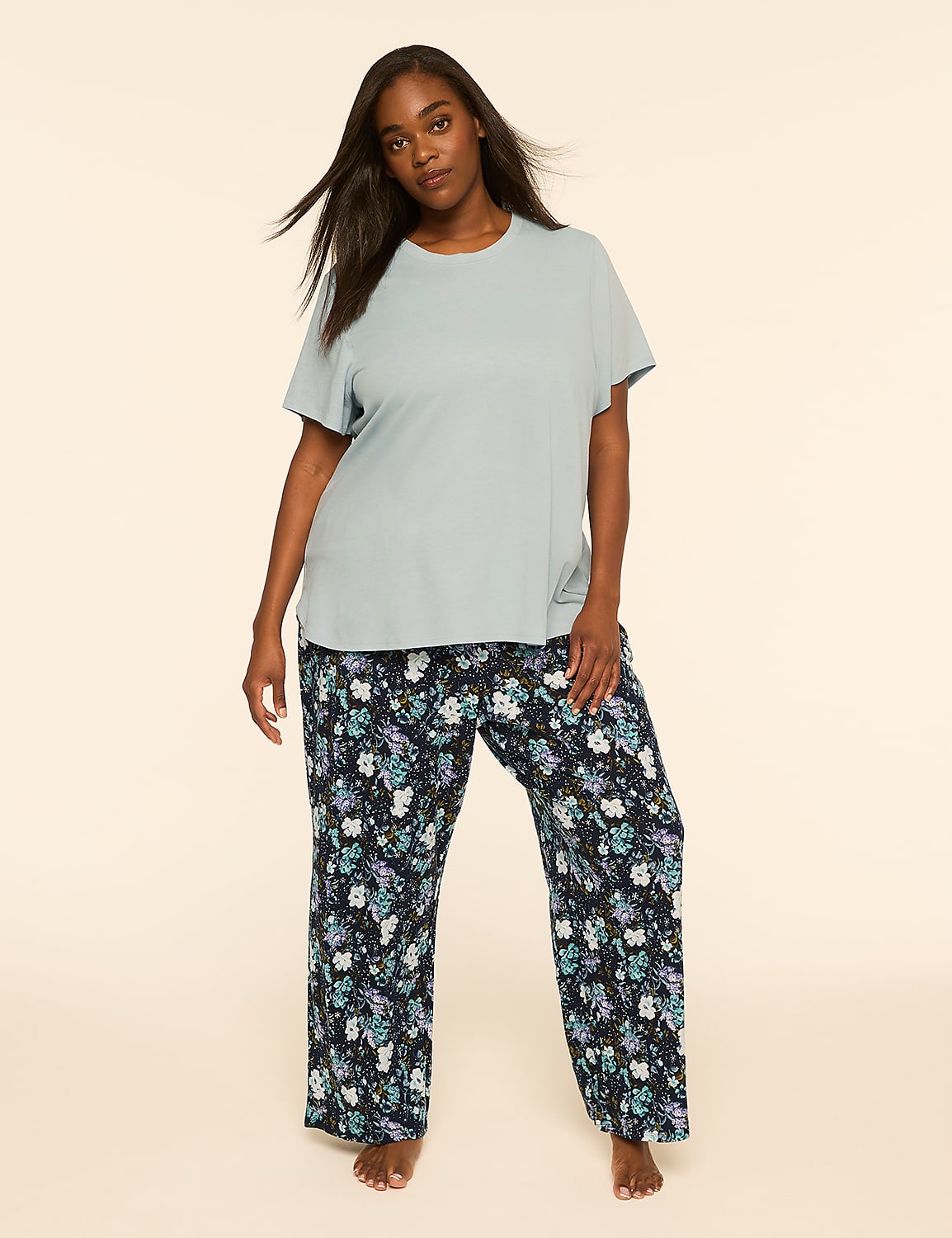 A woman wearing a light blue t-shirt and floral print pants stands against a plain, neutral background. Product Image 1