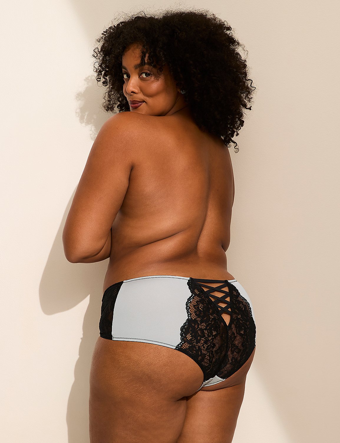 A woman with curly hair wearing light blue and black lace panties poses against a plain white wall. Product Image 3