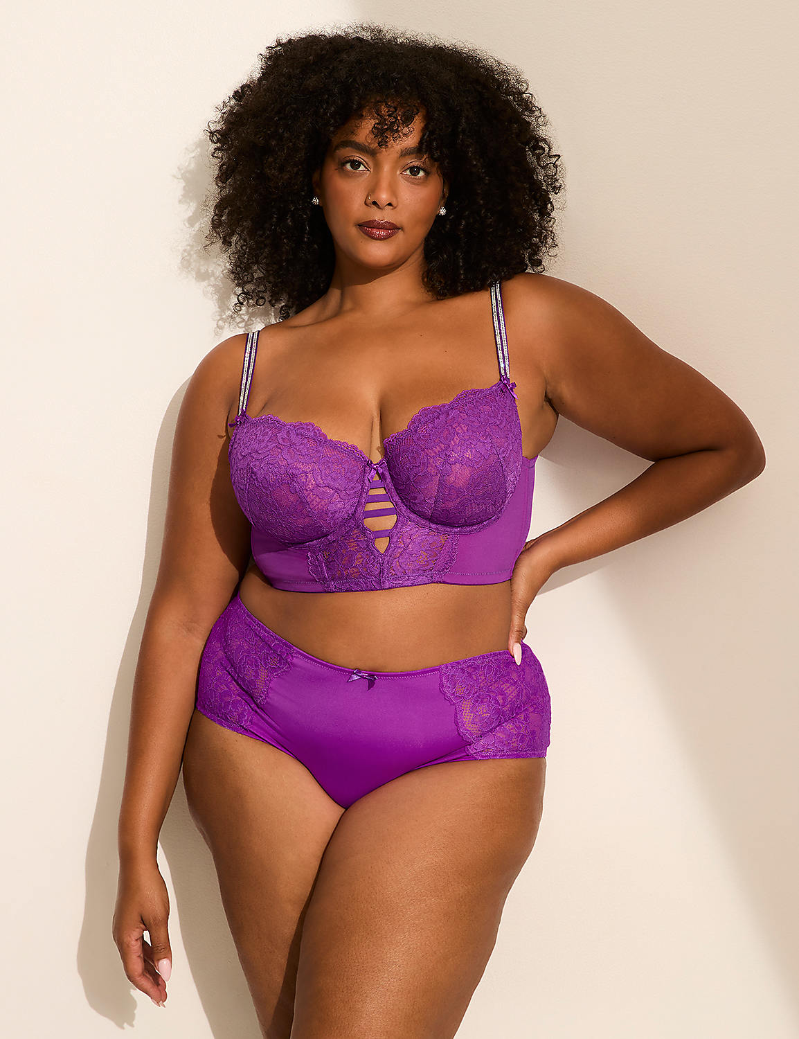 A woman with curly hair wearing a purple lace lingerie set poses against a plain white wall. Product Image 3