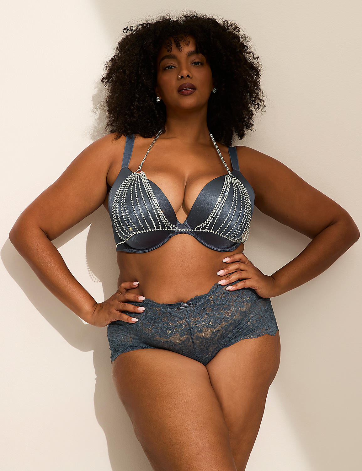 A woman with curly hair wearing a blue beaded lingerie set poses against a plain white wall. Product Image 3