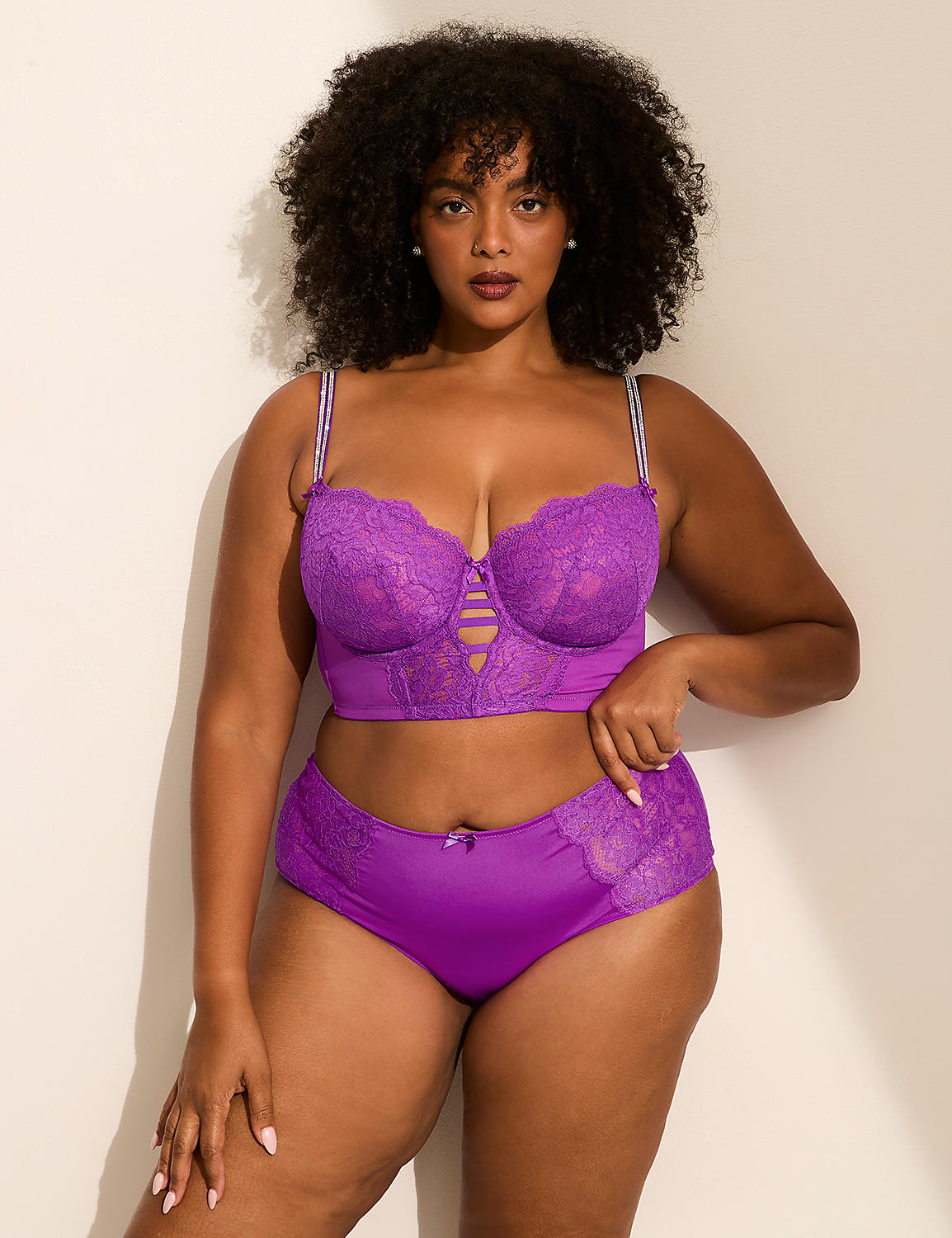 A woman with curly hair wearing a purple lace lingerie set poses against a plain white wall. Product Image 4