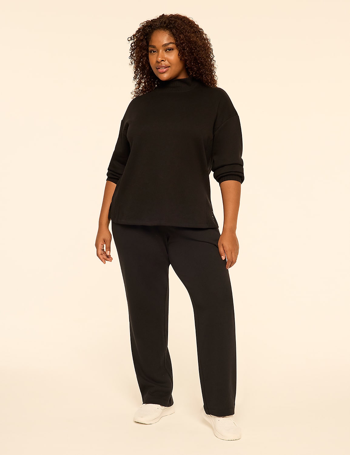 A woman with curly hair wearing a black long-sleeved top and matching black pants stands against a plain, light-colored background. Product Image 3