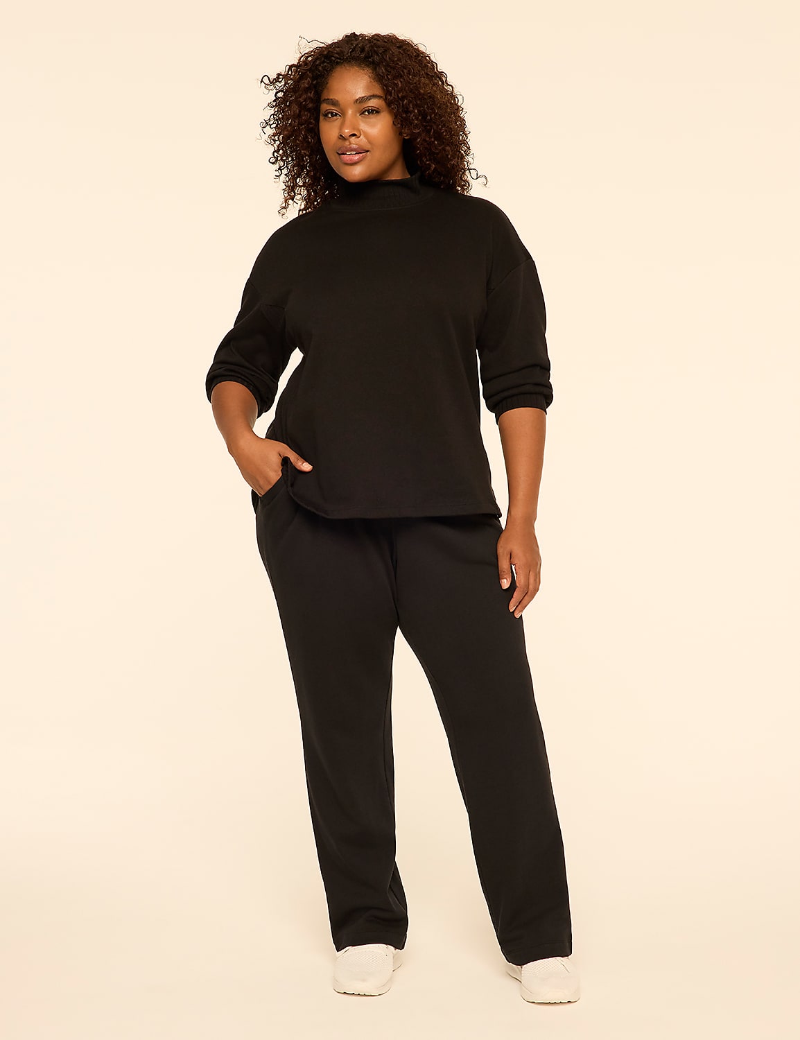 A woman with curly hair wearing a black long-sleeved top and matching black pants stands against a plain, light-colored background. Product Image 3