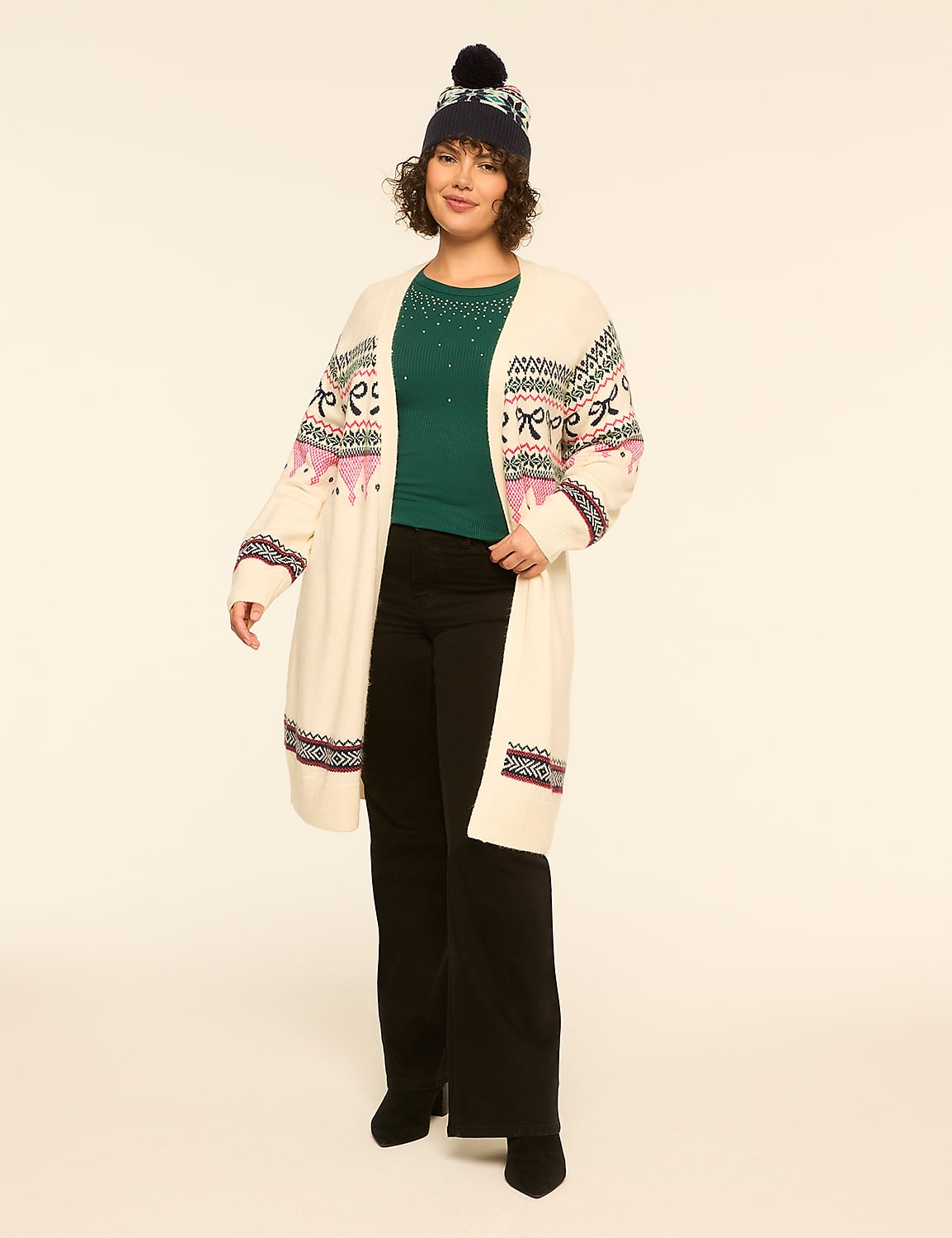 A woman wearing a patterned white cardigan, green top, black pants, and a beanie stands against a plain off-white background. Product Image 3