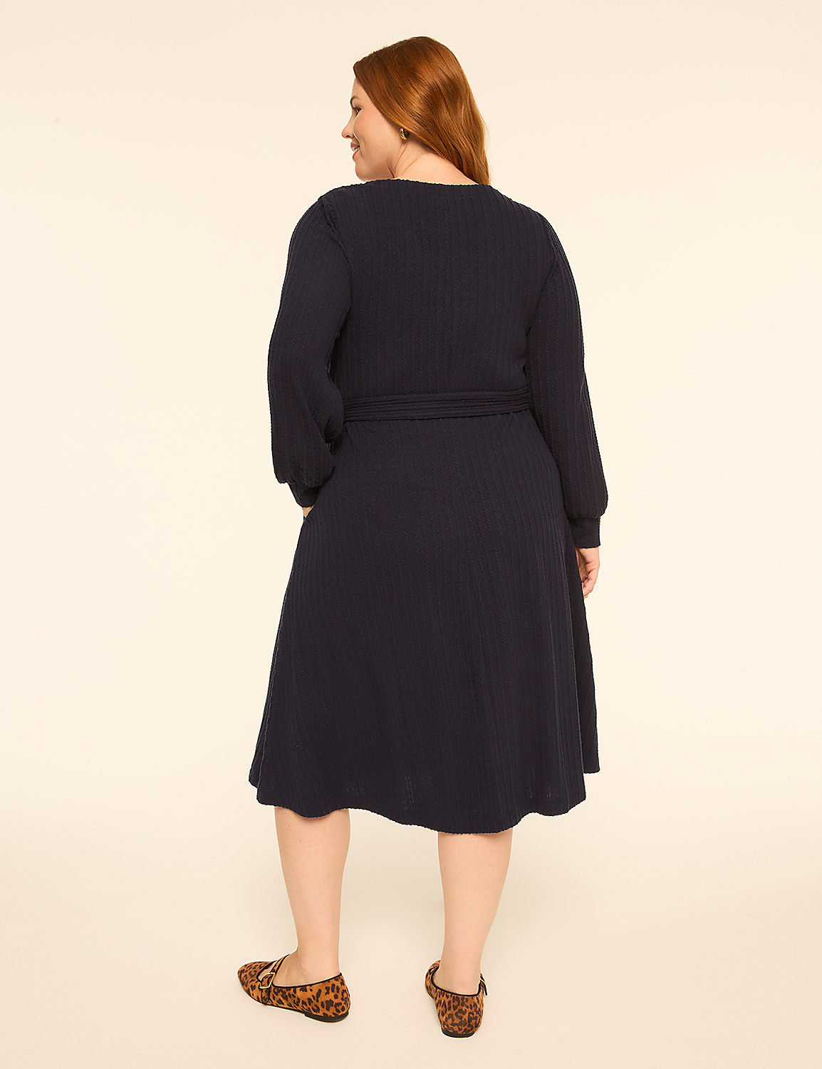 A woman with red hair wearing a navy blue long-sleeved dress and leopard print flats stands against a plain off-white background. Product Image 2