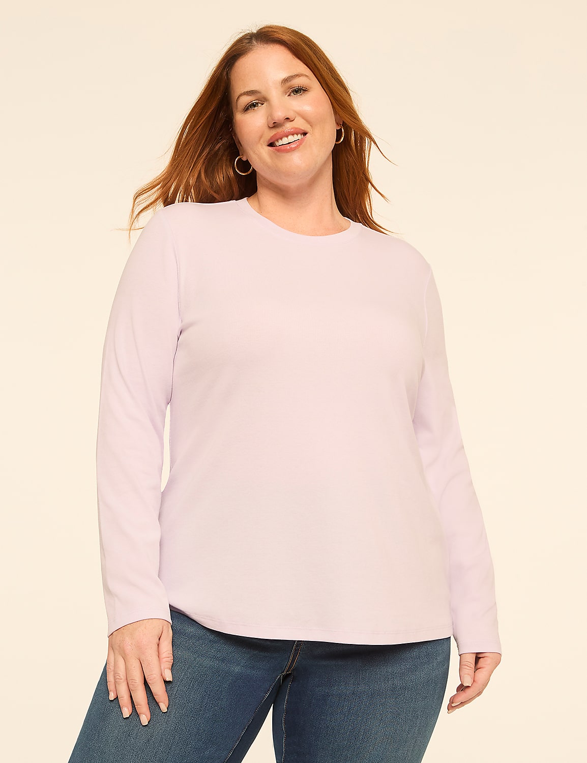 A smiling woman with red hair wearing a light purple long-sleeved shirt and blue jeans stands against a plain, off-white background. Product Image 1