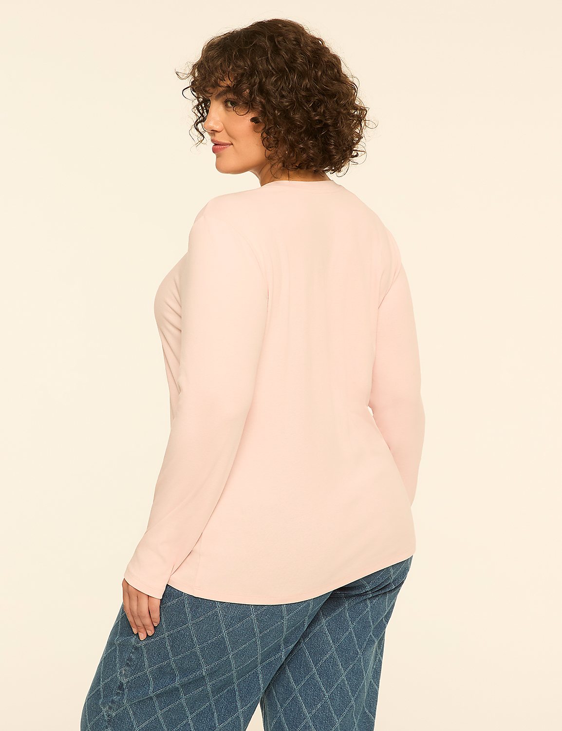 A woman with curly brown hair wearing a light pink long-sleeved top and blue patterned pants stands against a plain off-white background. Product Image 2