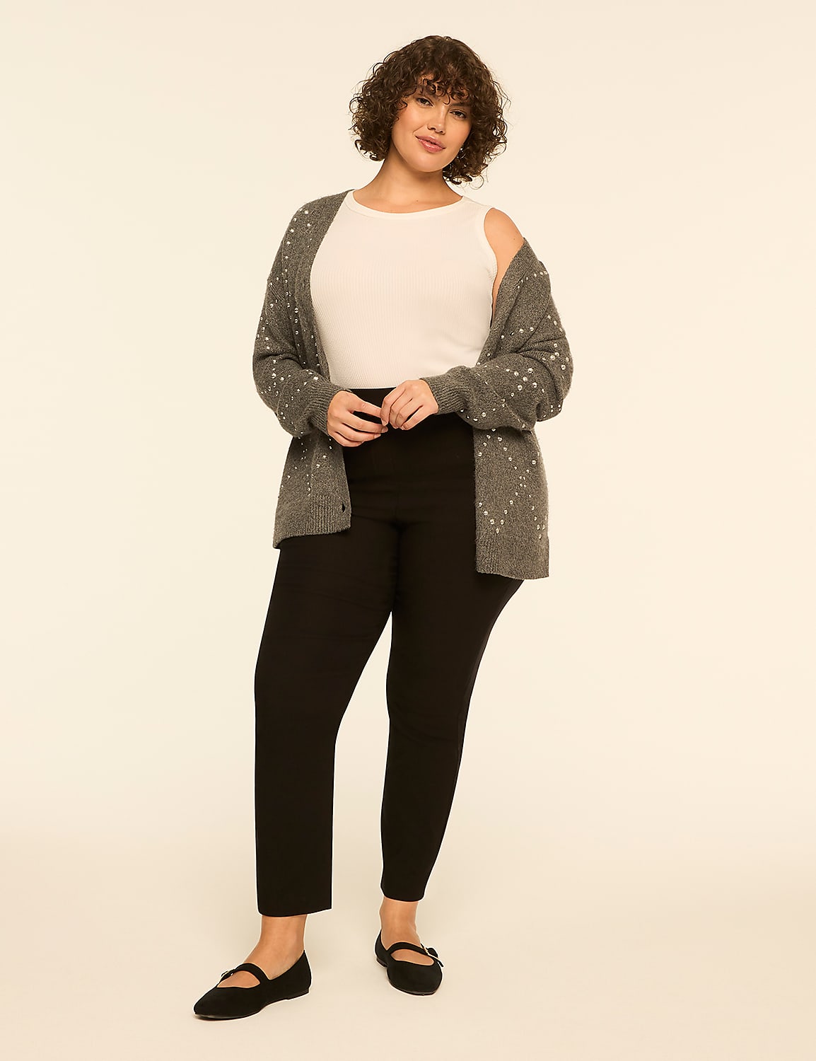 A woman wearing a white top, grey cardigan, and black trousers stands against a plain off-white background. Product Image 3