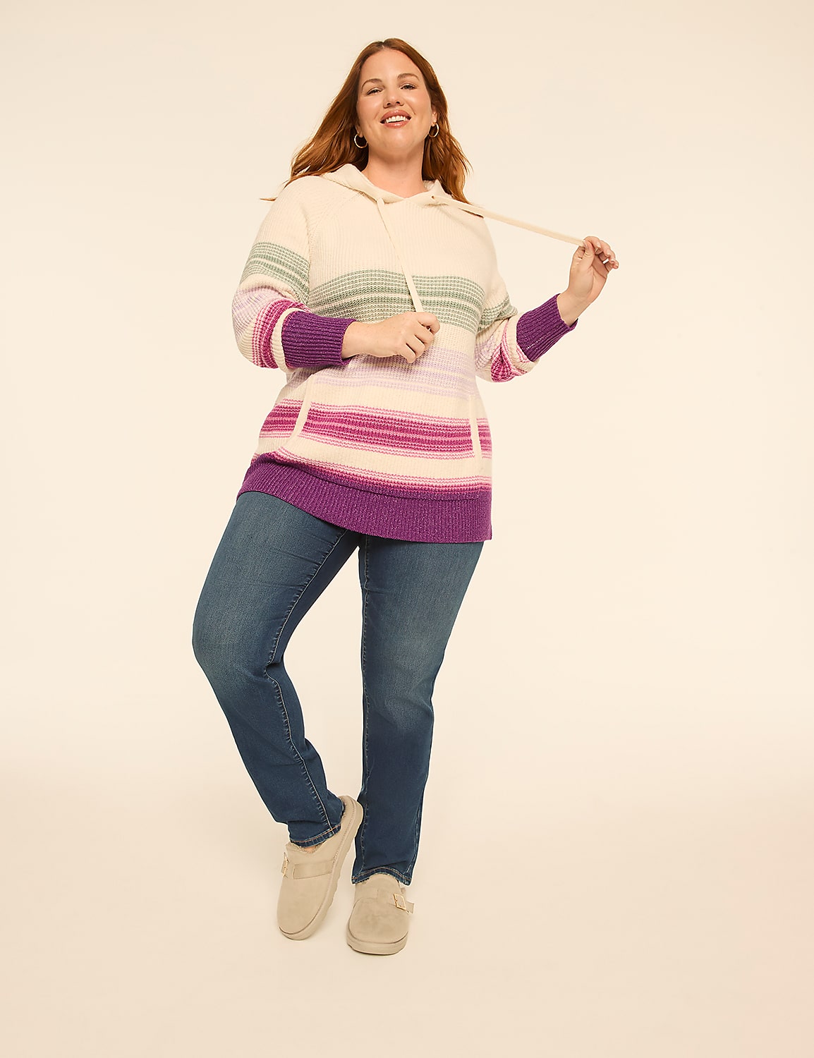 A smiling woman wearing a striped purple and white hoodie with blue jeans stands against a plain, light-colored background. Product Image 3