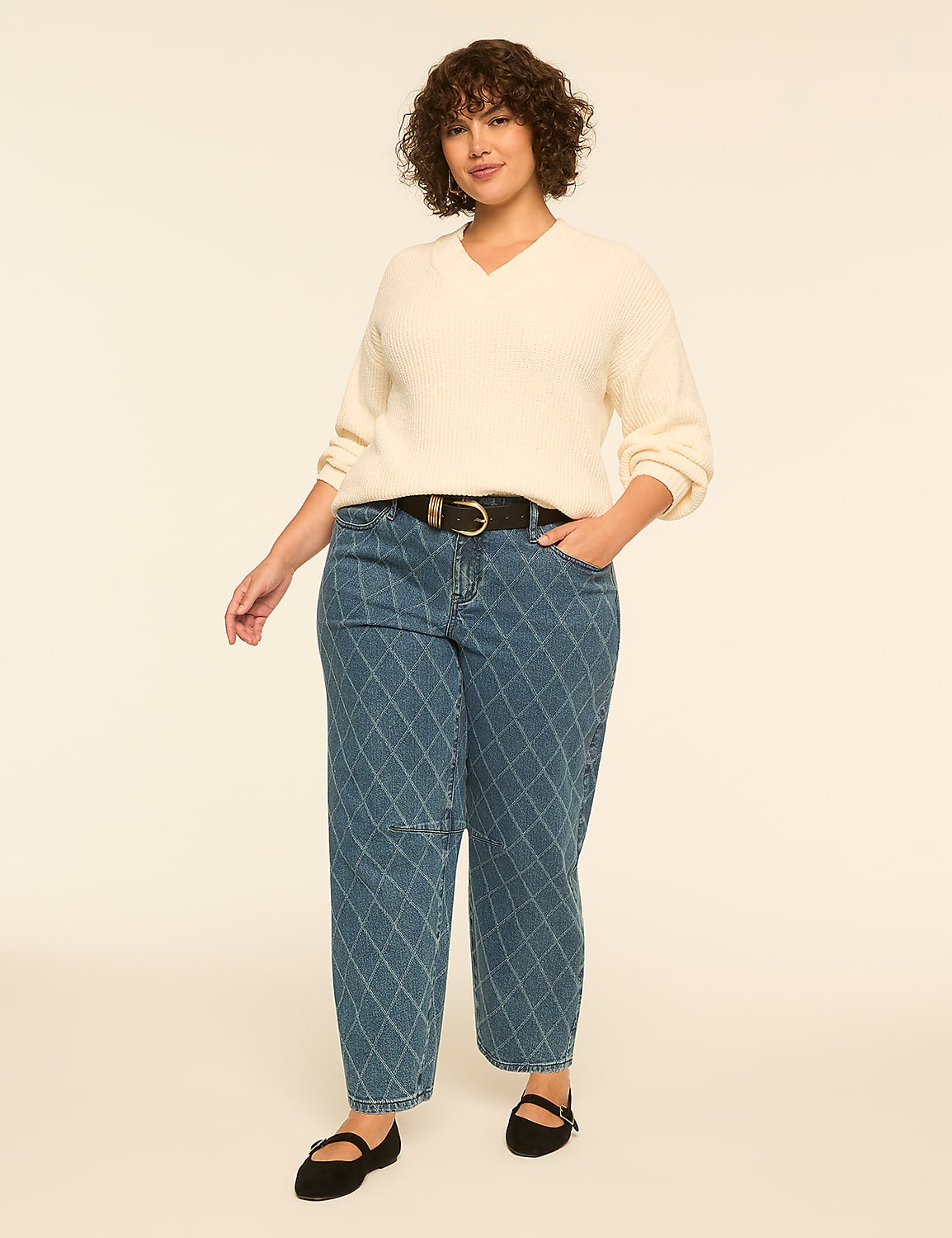 A woman wearing a cream-colored v-neck sweater and quilted blue jeans stands against a plain, light-colored background. Product Image 3