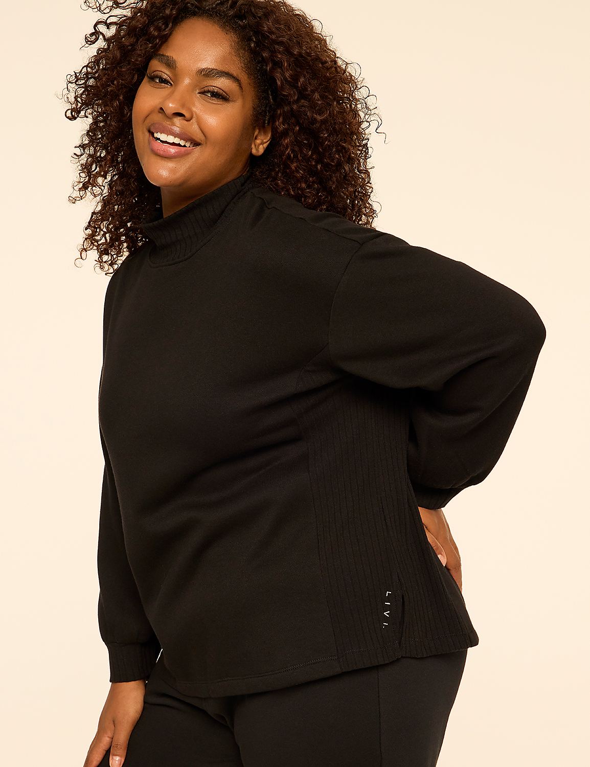 A smiling woman with curly hair wearing a black long-sleeved top stands against a plain, light-colored background. Product Image 4