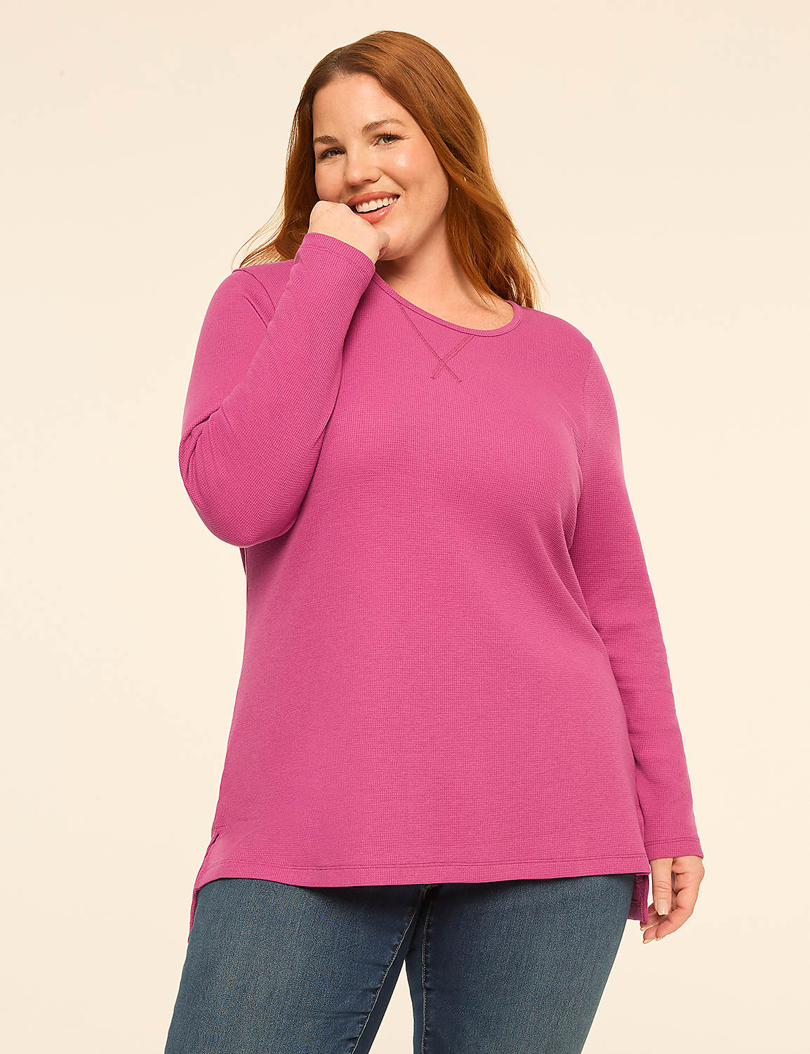 A smiling woman with red hair wearing a bright pink long-sleeved shirt and blue jeans stands against a plain, light-colored background. Product Image 1