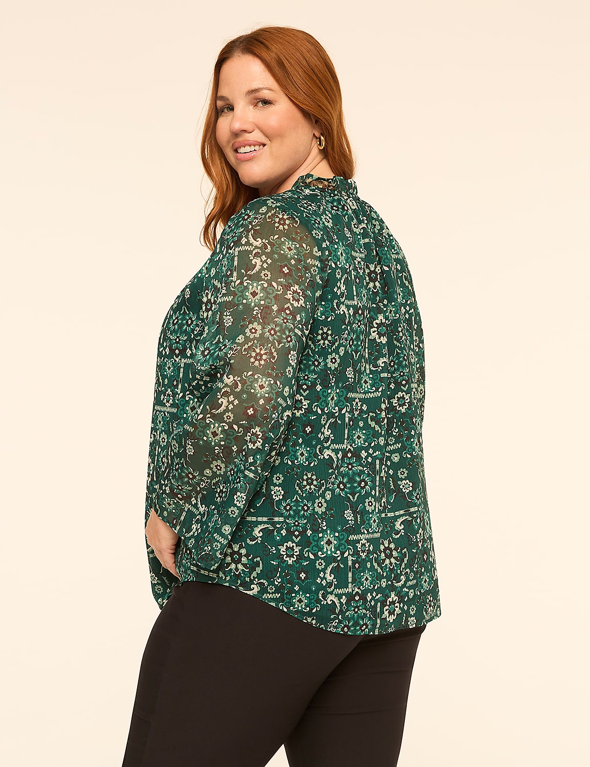 A woman with red hair wearing a green floral blouse and black pants stands against a plain, light-colored background. Product Image 2