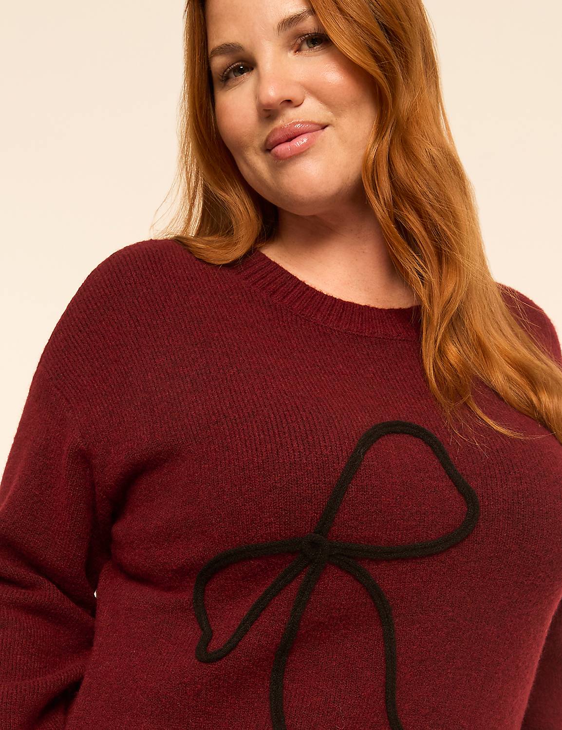 A woman with long red hair wearing a maroon sweater with a black bow detail poses against a plain, light-colored background. Product Image 4