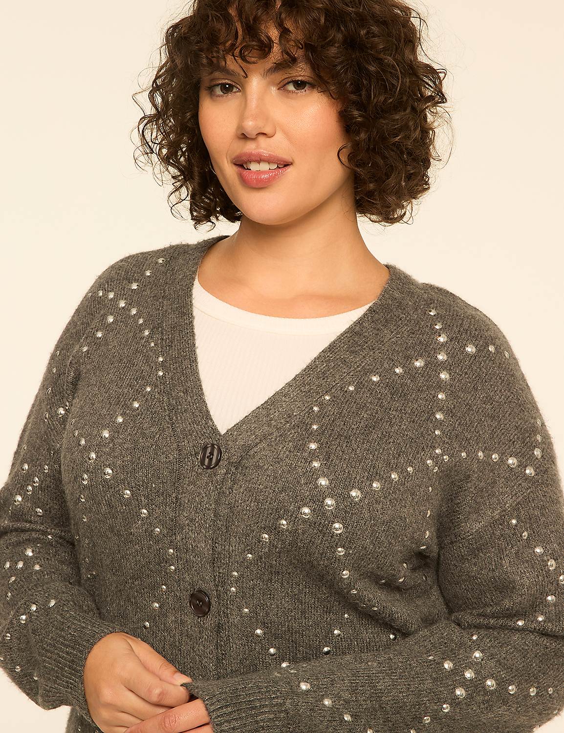 A woman with curly brown hair wears a grey studded cardigan over a white top against a plain, light-colored background. Product Image 4