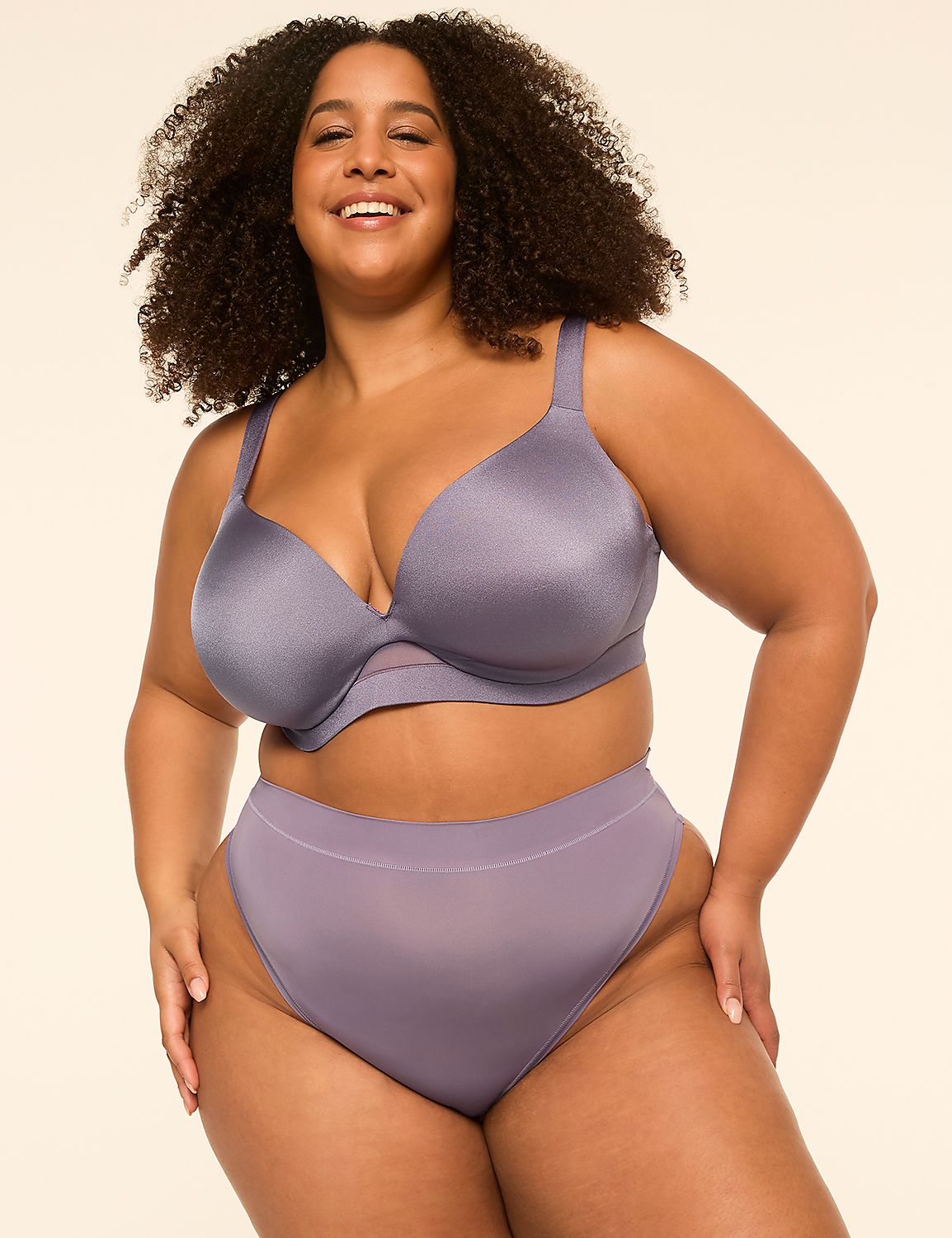 A smiling woman with curly hair wears a purple lingerie set against a plain, light-colored background. Product Image 4
