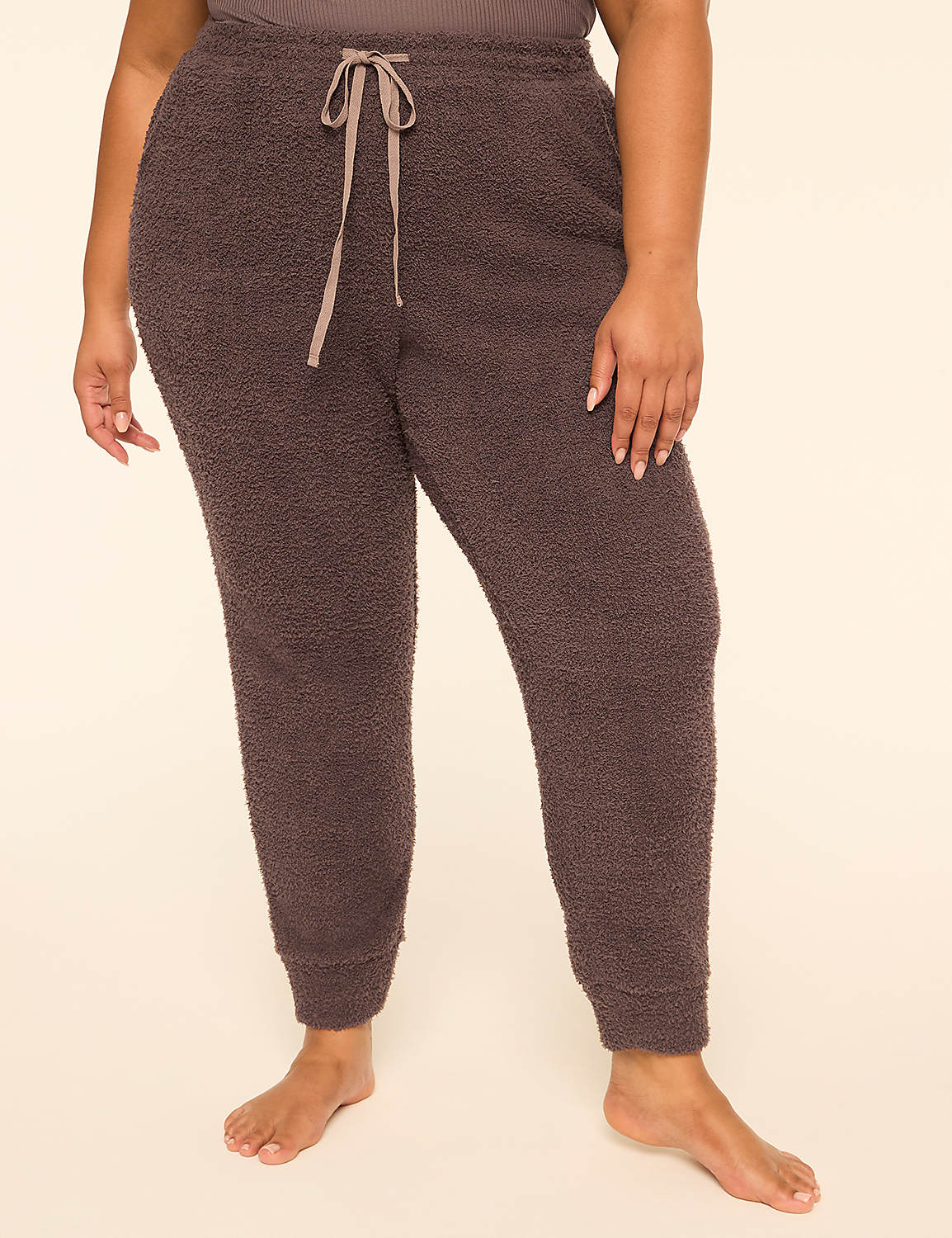 A person wearing dark brown fuzzy jogger pants stands against a plain, light beige background. Product Image 1