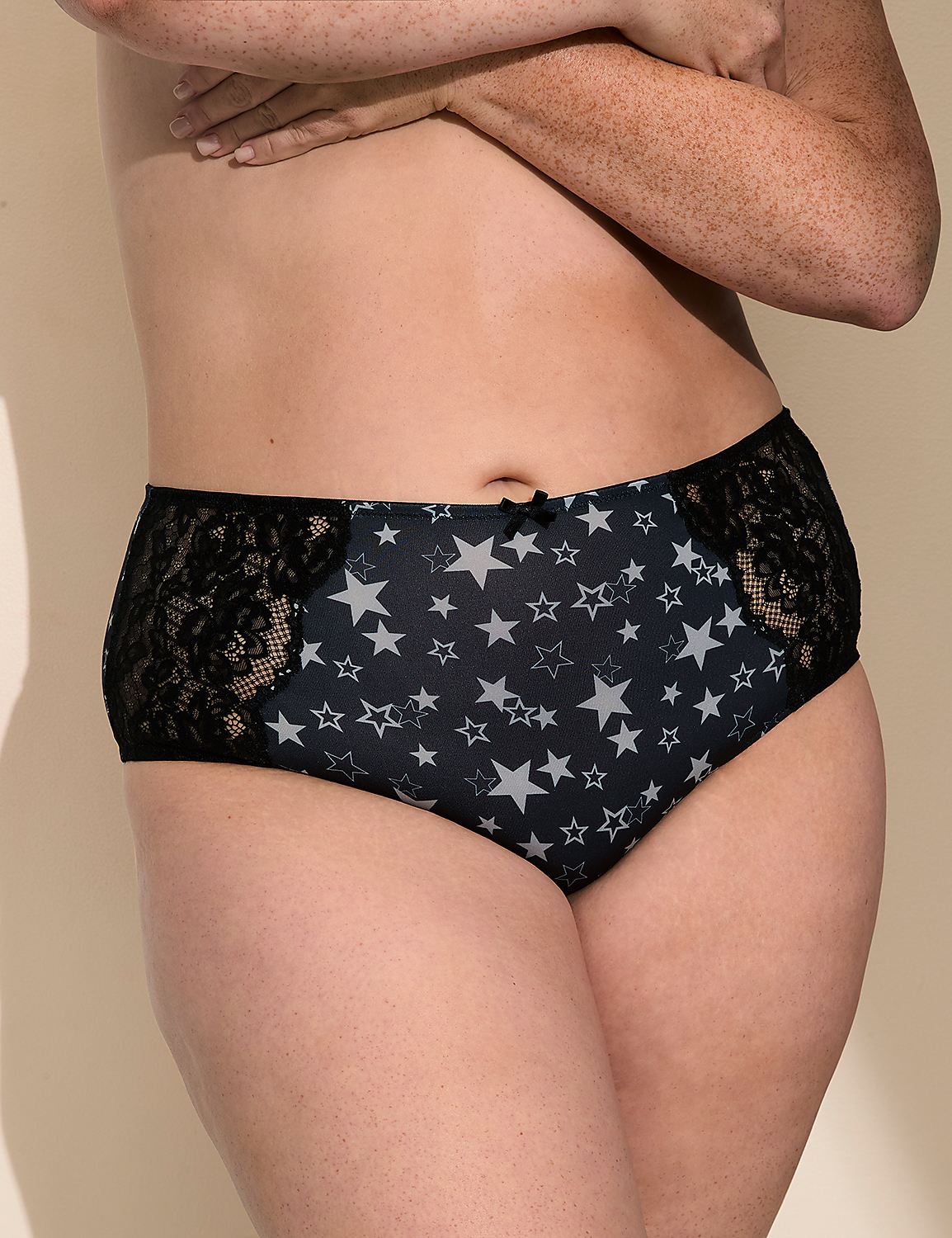 A person wears navy blue star-patterned panties with black lace panels against a plain, light-colored background. Product Image 1