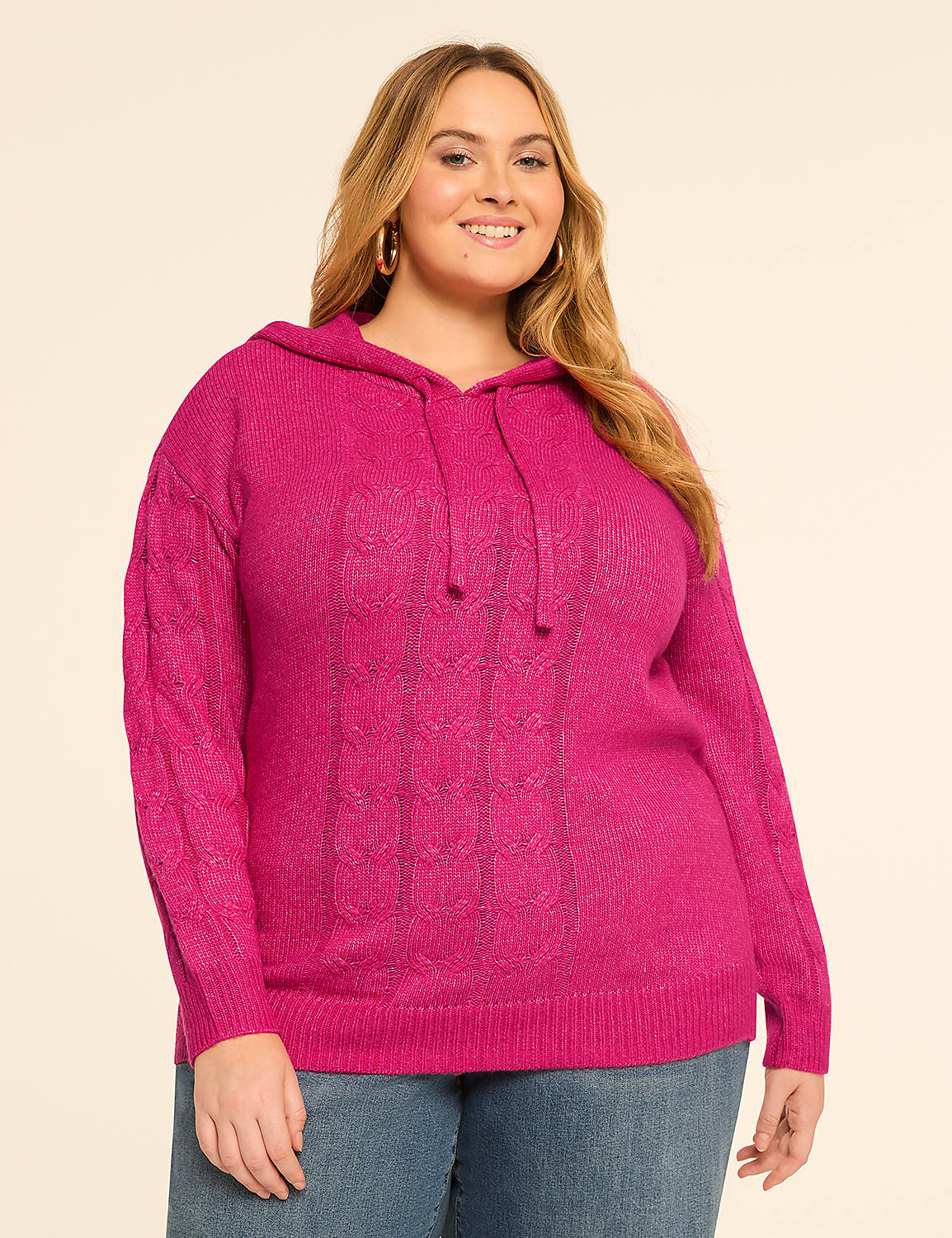 A smiling woman in a pink cable-knit hoodie stands against a plain, light-colored background. Product Image 1