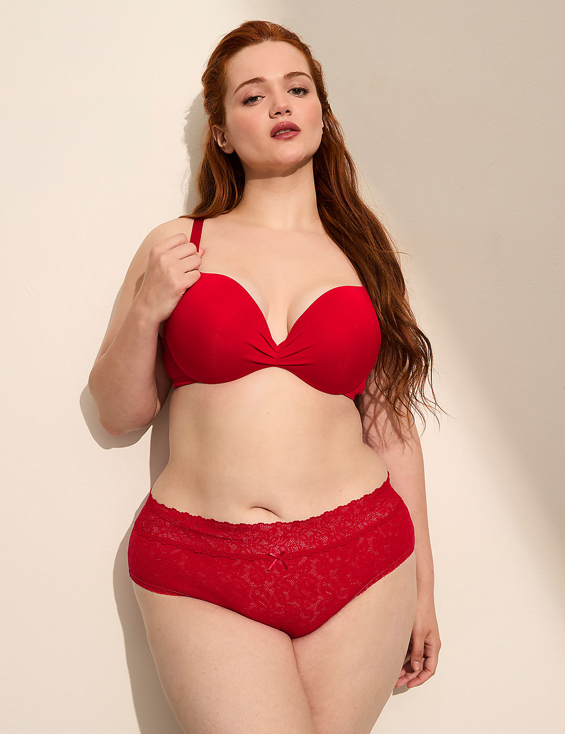 A woman with red hair wears a red bra, leaning against a plain, light-colored wall. Product Image 4