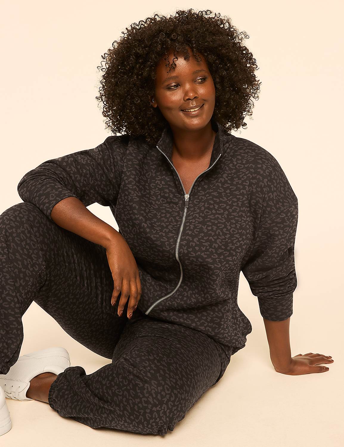 A woman with dark, curly hair and a leopard-print tracksuit sits on a plain, light-colored background. Product Image 3